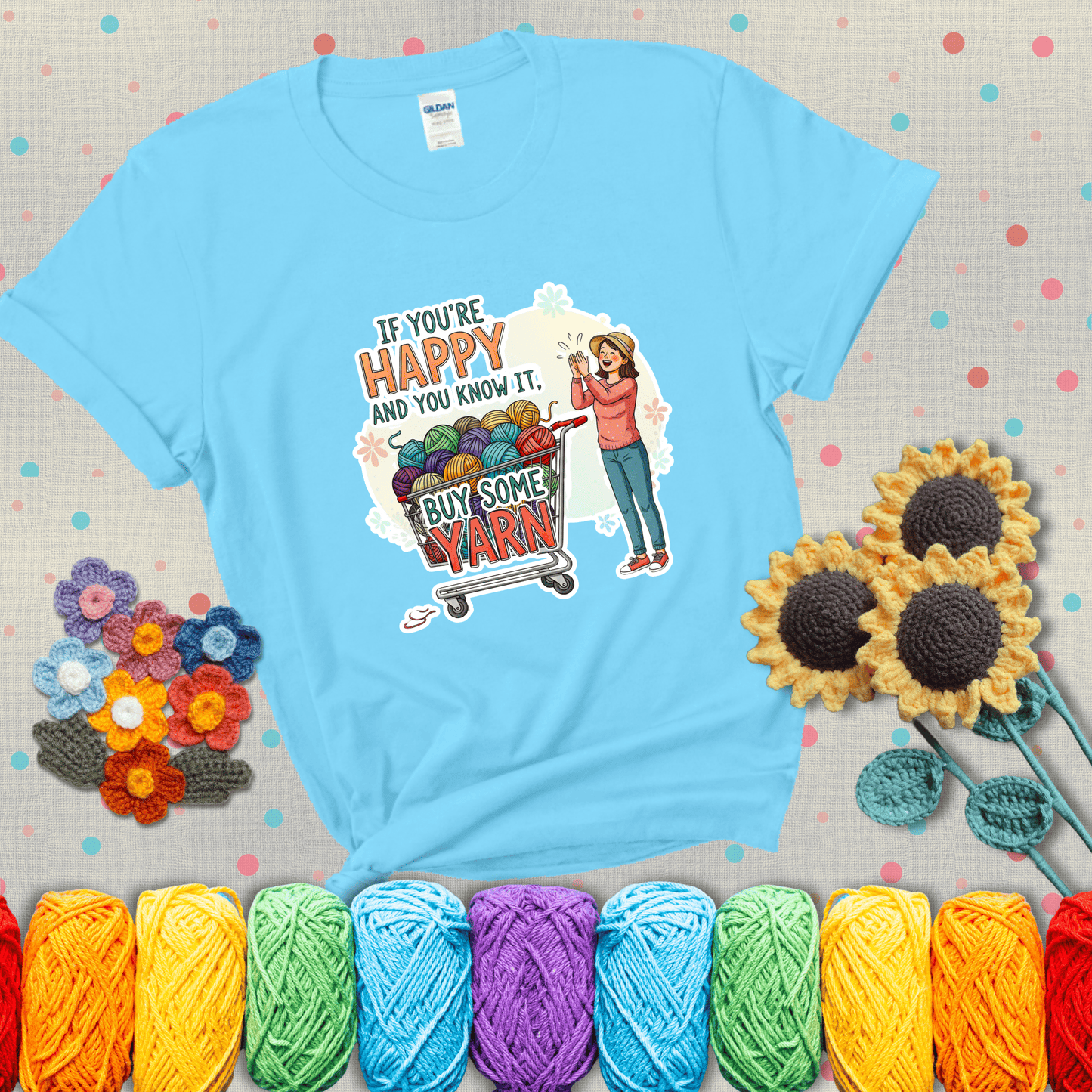 Woman clapping beside a shopping cart overflowing with colorful yarn balls, styled with cheerful pastel accents and bold playful lettering showing a light blue tee with grey sunflower background