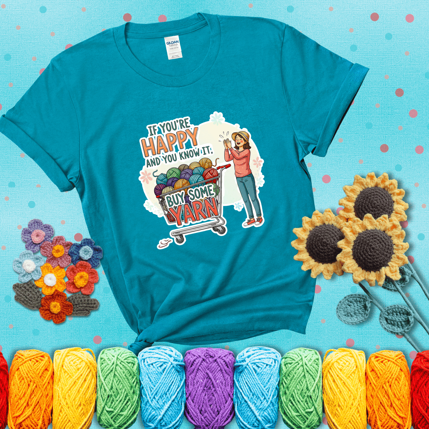 Woman clapping beside a shopping cart overflowing with colorful yarn balls, styled with cheerful pastel accents and bold playful lettering showing a blue-green tee with a teal sunflower background