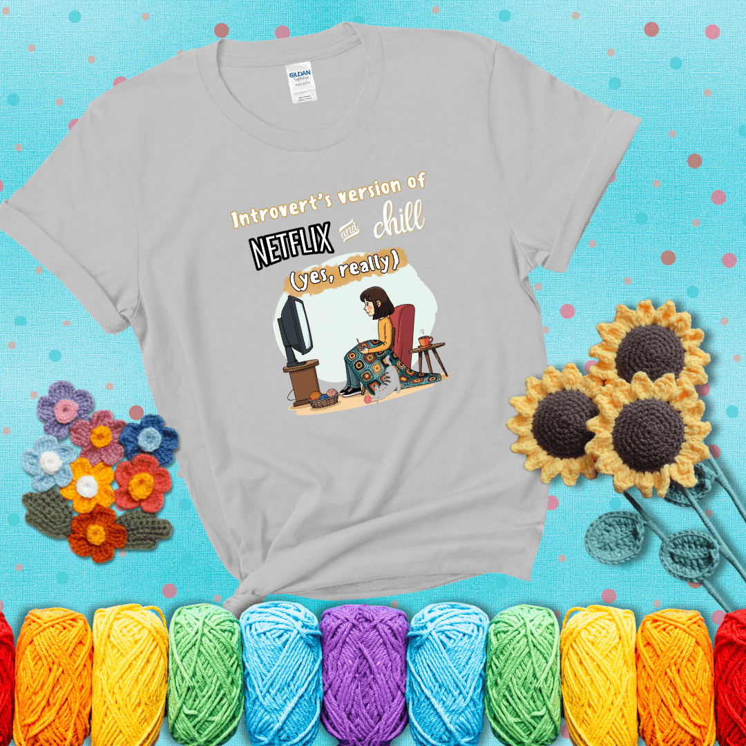 A girl with a crochet hook sits under a granny square blanket watching TV, with yarn, a coffee mug, and a cat at her feet. Text says “Introvert’s version of Netflix and chill (yes, really)," showing a light grey tee with a teal sunflower background