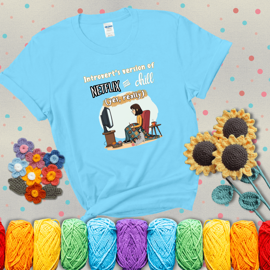 A girl with a crochet hook sits under a granny square blanket watching TV, with yarn, a coffee mug, and a cat at her feet. Text says “Introvert’s version of Netflix and chill (yes, really)," showing a light blue tee with grey sunflower background