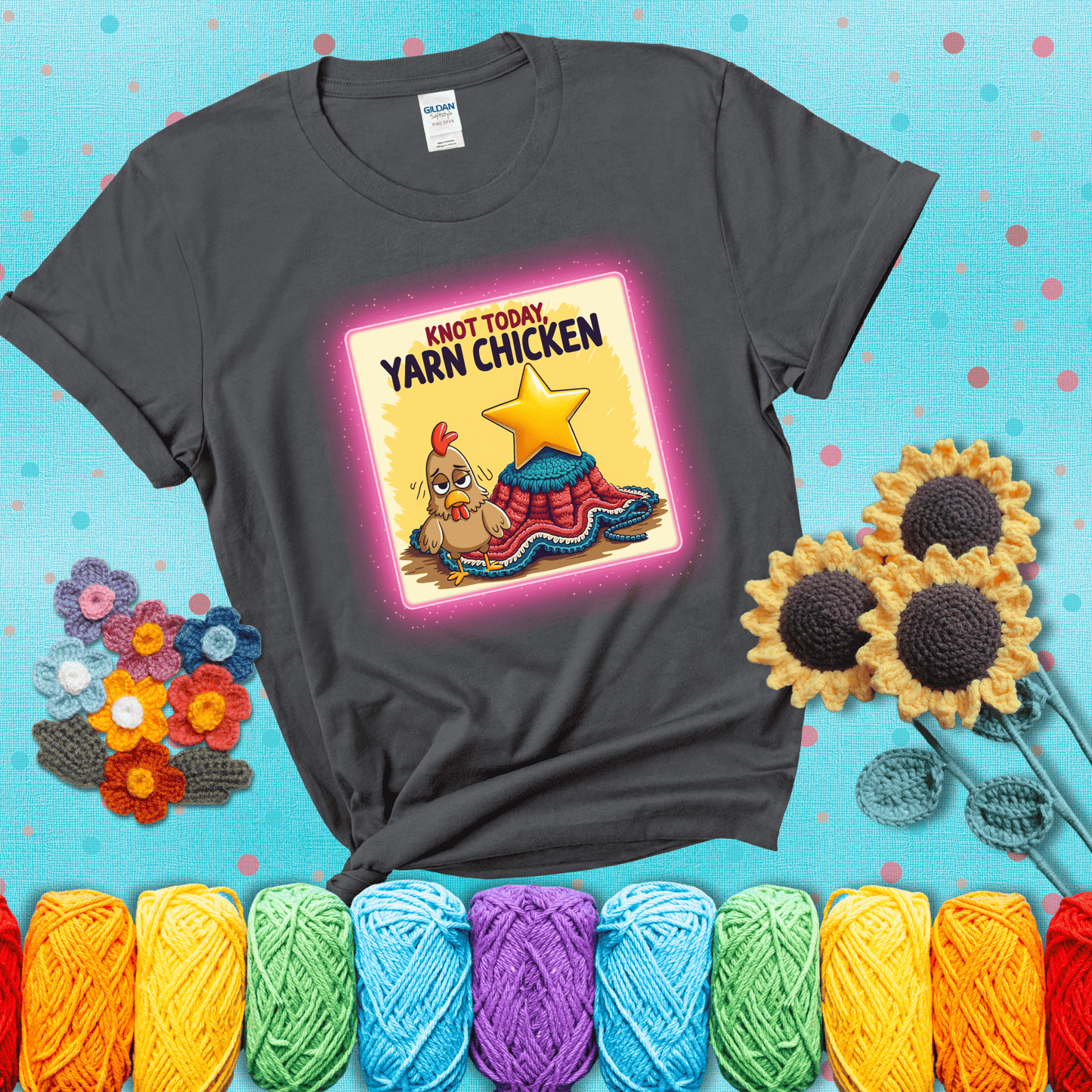 A frazzled cartoon chicken stands next to a nearly-finished project with minimal yarn left, with the phrase “Knot Today, Yarn Chicken” above, showing a dark grey tee with a teal sunflower background