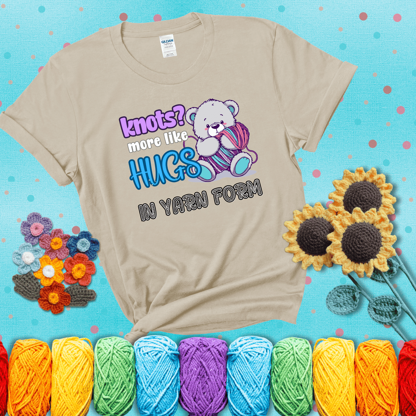 Cute teddy bear holding colorful yarn ball with hearts. Text reads: “Knots? More Like Hugs in Yarn Form.” Perfect for cozy gift-givers and yarn lovers, showing a beige tee with a teal sunflower background