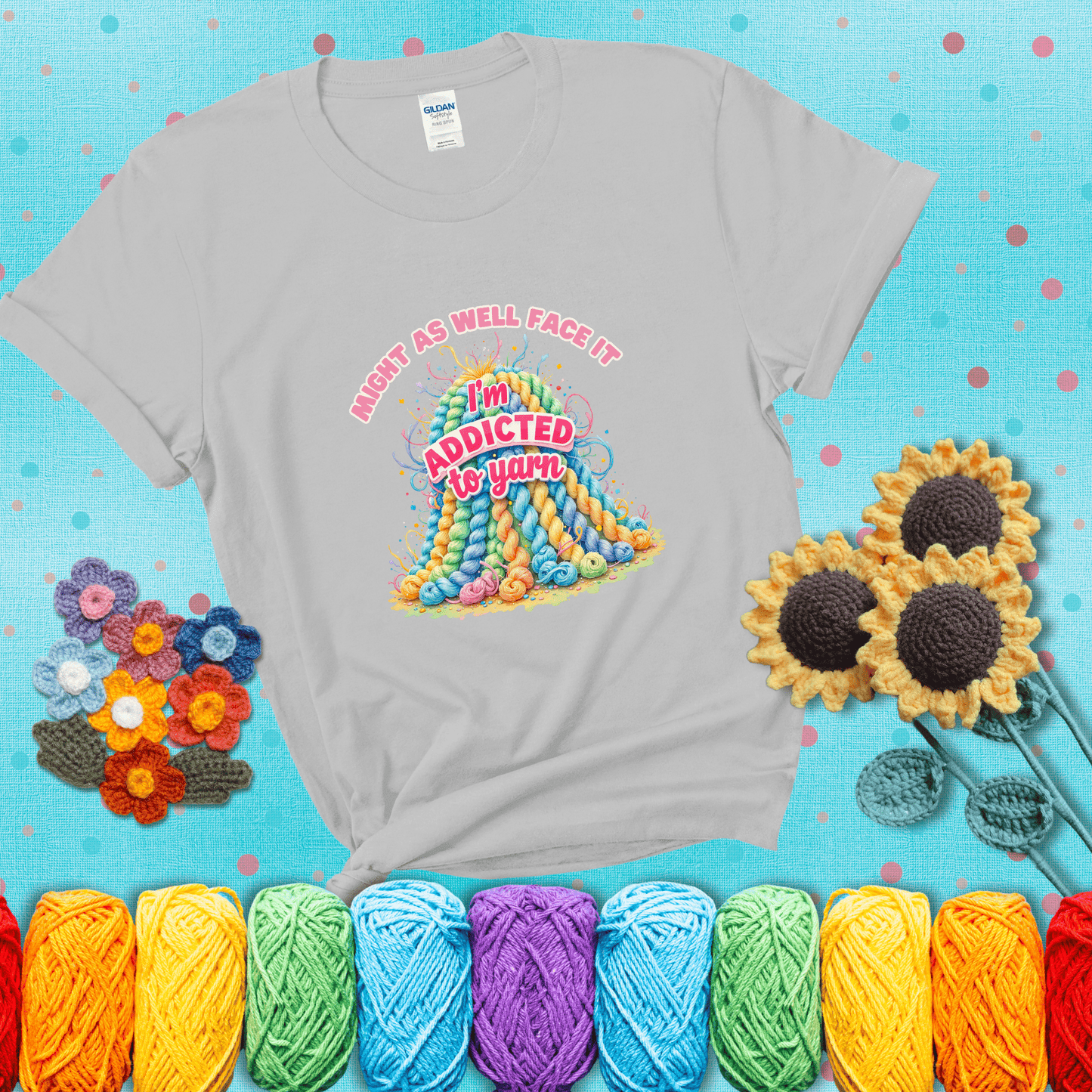 Colorful mountain of pastel yarn hanks with the phrase “Might as well face it, I’m addicted to yarn” in playful pink and red lettering showing a light grey tee with a teal sunflower background