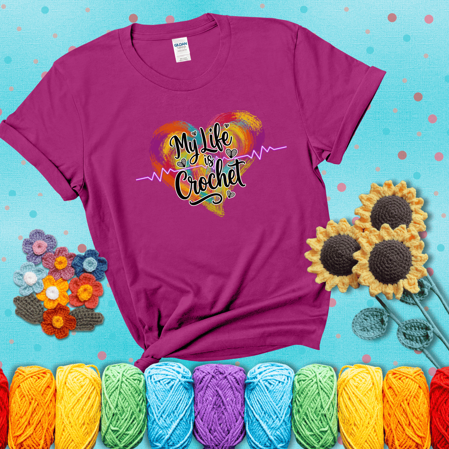 Colorful heart with an EKG line and text: “My Life is Crochet” in bold script showing a magenta tee with a teal sunflower background