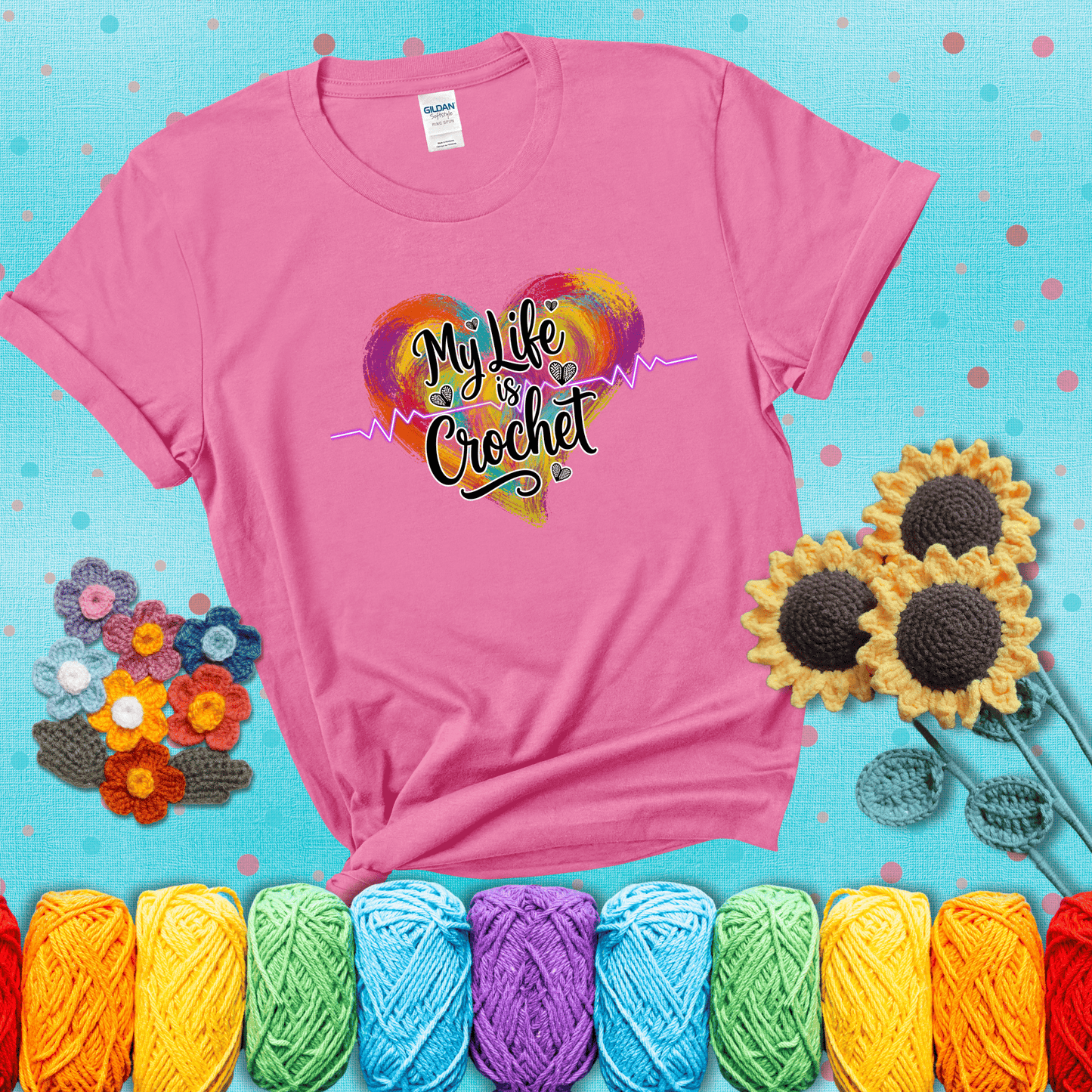 Colorful heart with an EKG line and text: “My Life is Crochet” in bold script showing a pink tee with a teal sunflower background