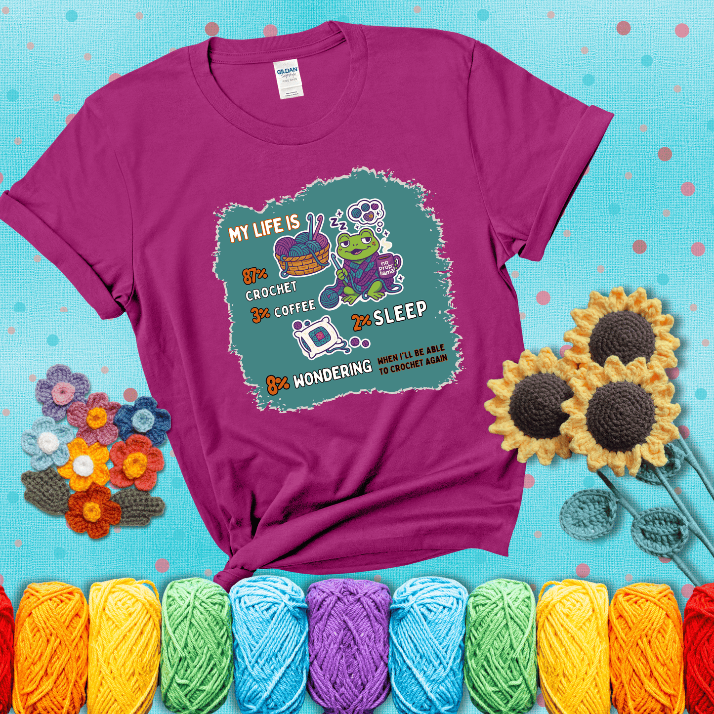 A relaxed frog crocheting while sipping coffee, surrounded by yarn and dreaming of more yarn. Includes whimsical text dividing life into percentages: 87% crochet, 3% coffee, 2% sleep, 8% wondering when to crochet again showing a light purple tee with a teal sunflower background