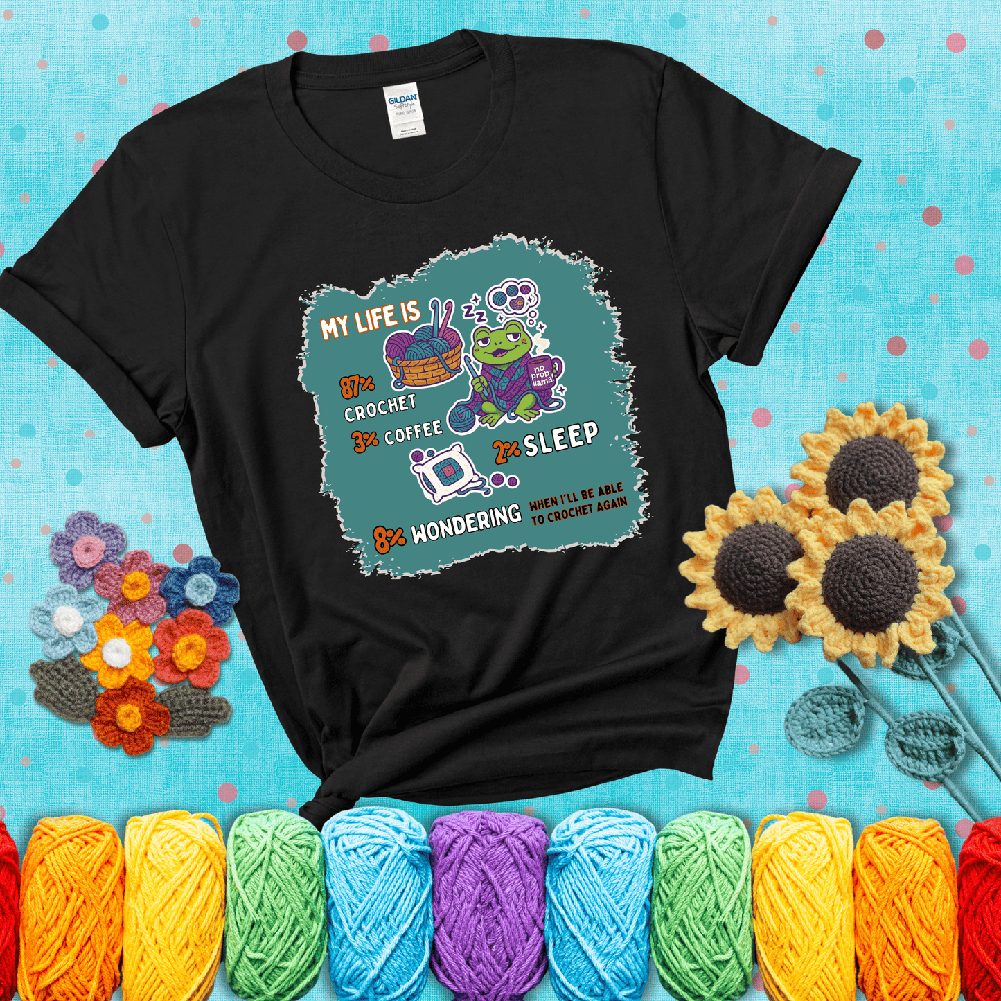 A relaxed frog crocheting while sipping coffee, surrounded by yarn and dreaming of more yarn. Includes whimsical text dividing life into percentages: 87% crochet, 3% coffee, 2% sleep, 8% wondering when to crochet again showing a black tee with a teal sunflower background