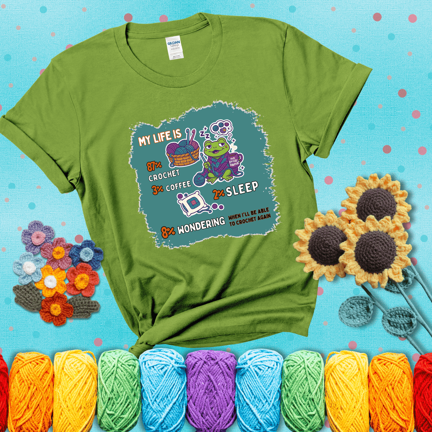 A relaxed frog crocheting while sipping coffee, surrounded by yarn and dreaming of more yarn. Includes whimsical text dividing life into percentages: 87% crochet, 3% coffee, 2% sleep, 8% wondering when to crochet again showing a bright green tee with a teal sunflower background