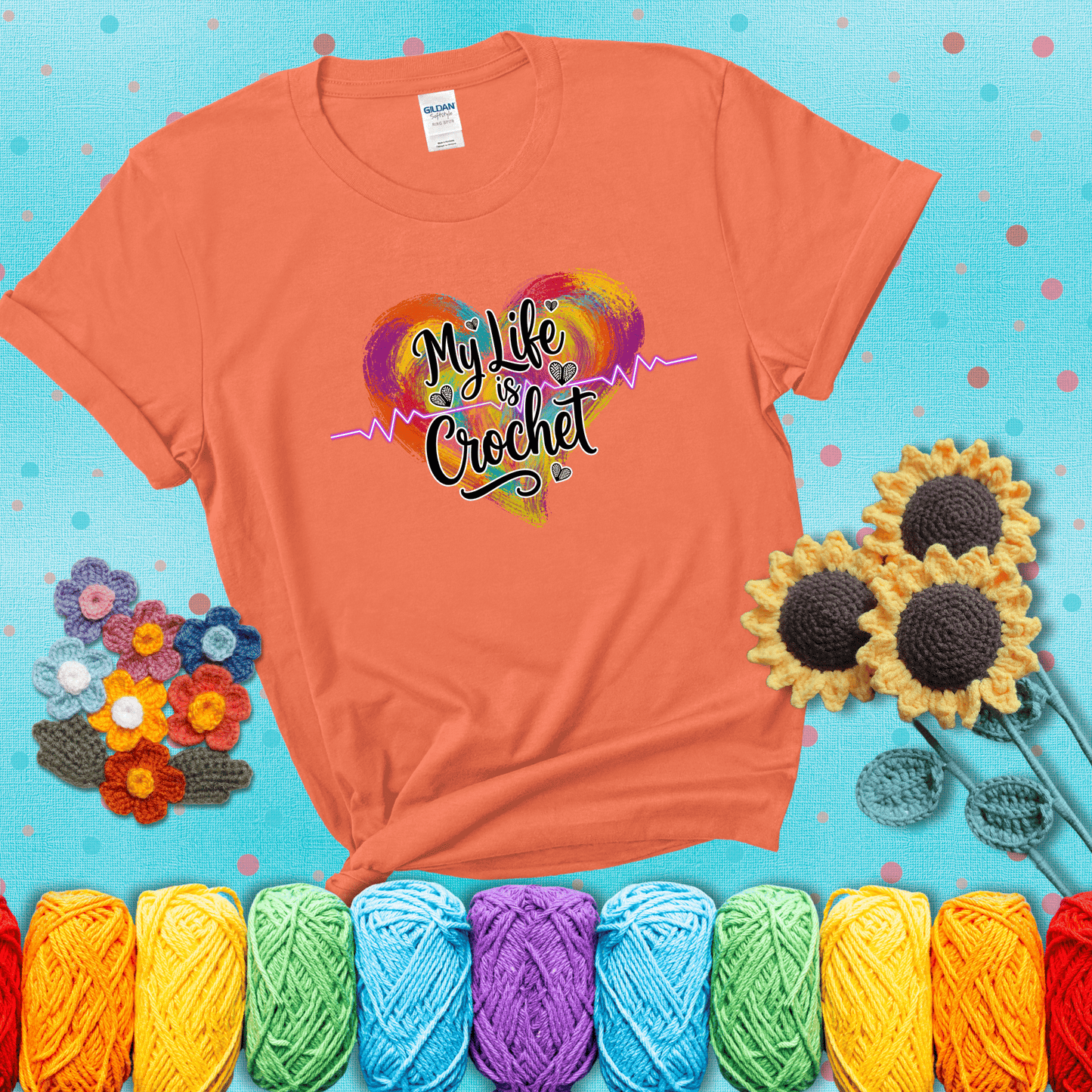 Colorful heart with an EKG line and text: “My Life is Crochet” in bold script showing a light orange tee with a teal sunflower background