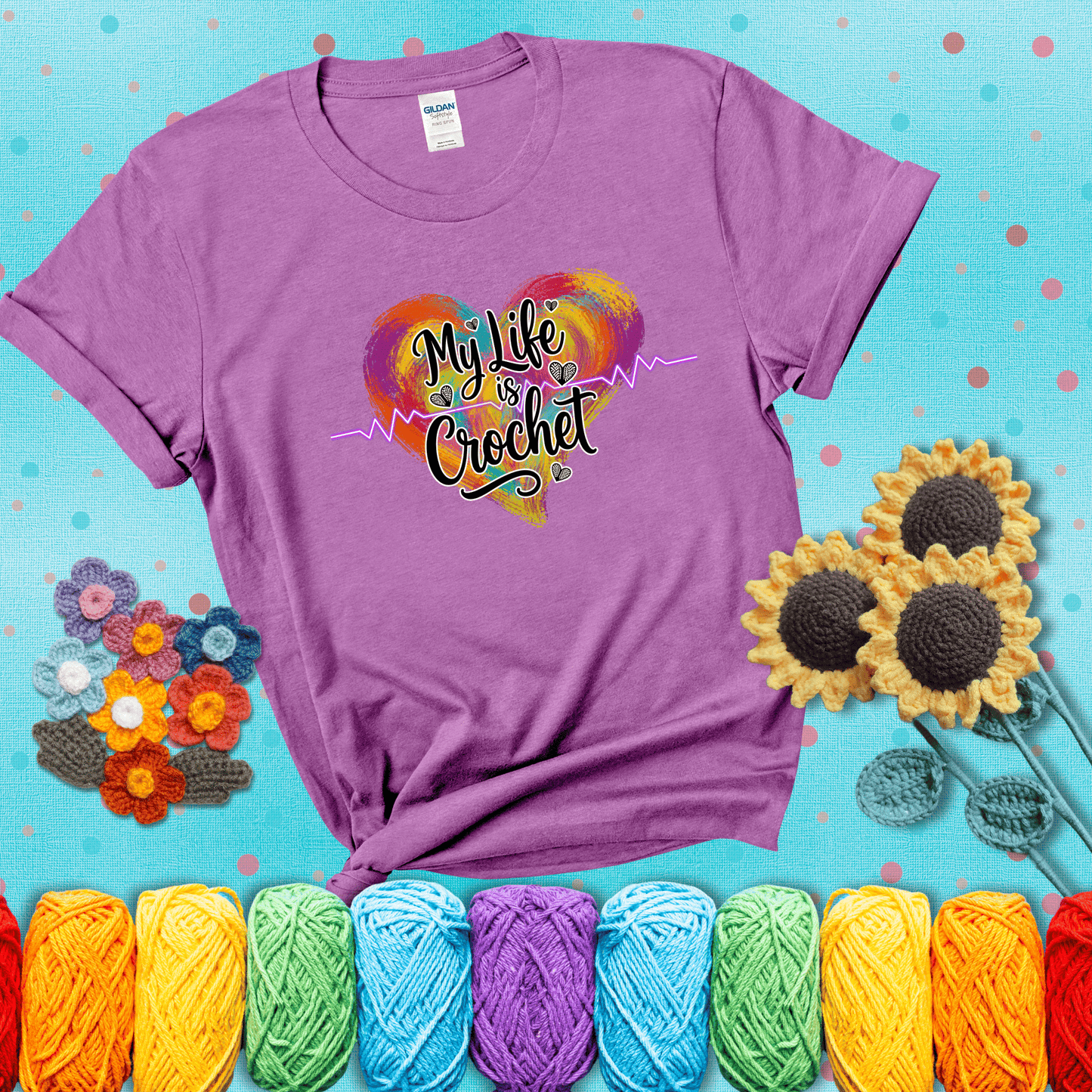 Colorful heart with an EKG line and text: “My Life is Crochet” in bold script showing a light purple tee with a teal sunflower background