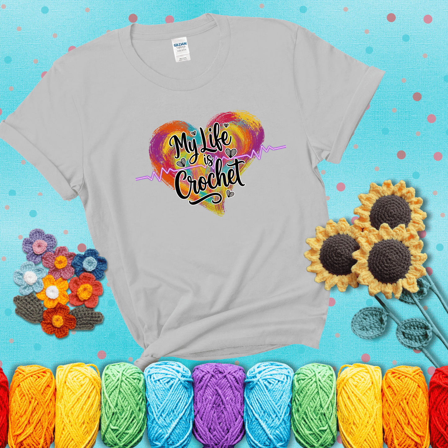 Colorful heart with an EKG line and text: “My Life is Crochet” in bold script showing a light grey tee with a teal sunflower background