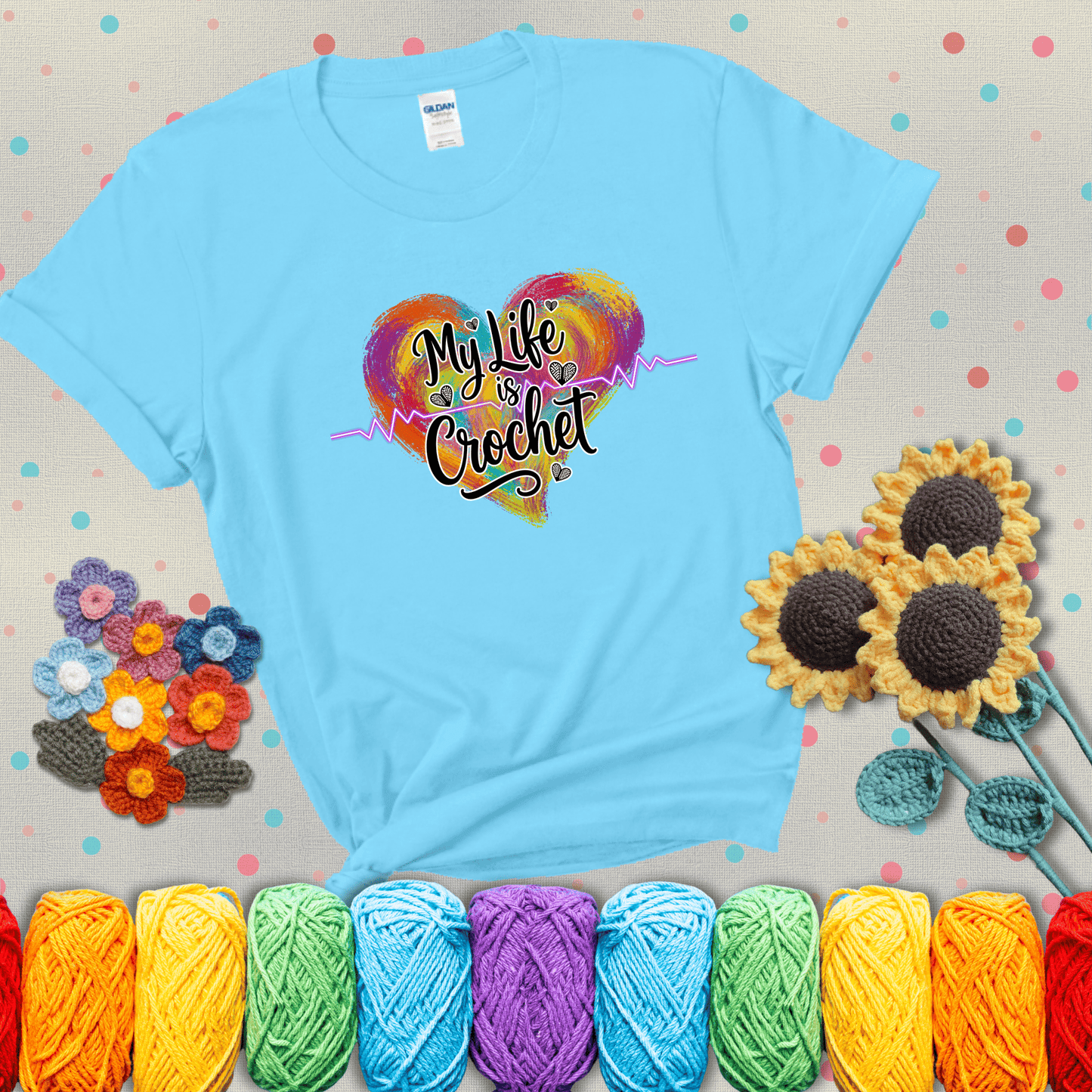 Colorful heart with an EKG line and text: “My Life is Crochet” in bold script showing a light blue tee with grey sunflower background