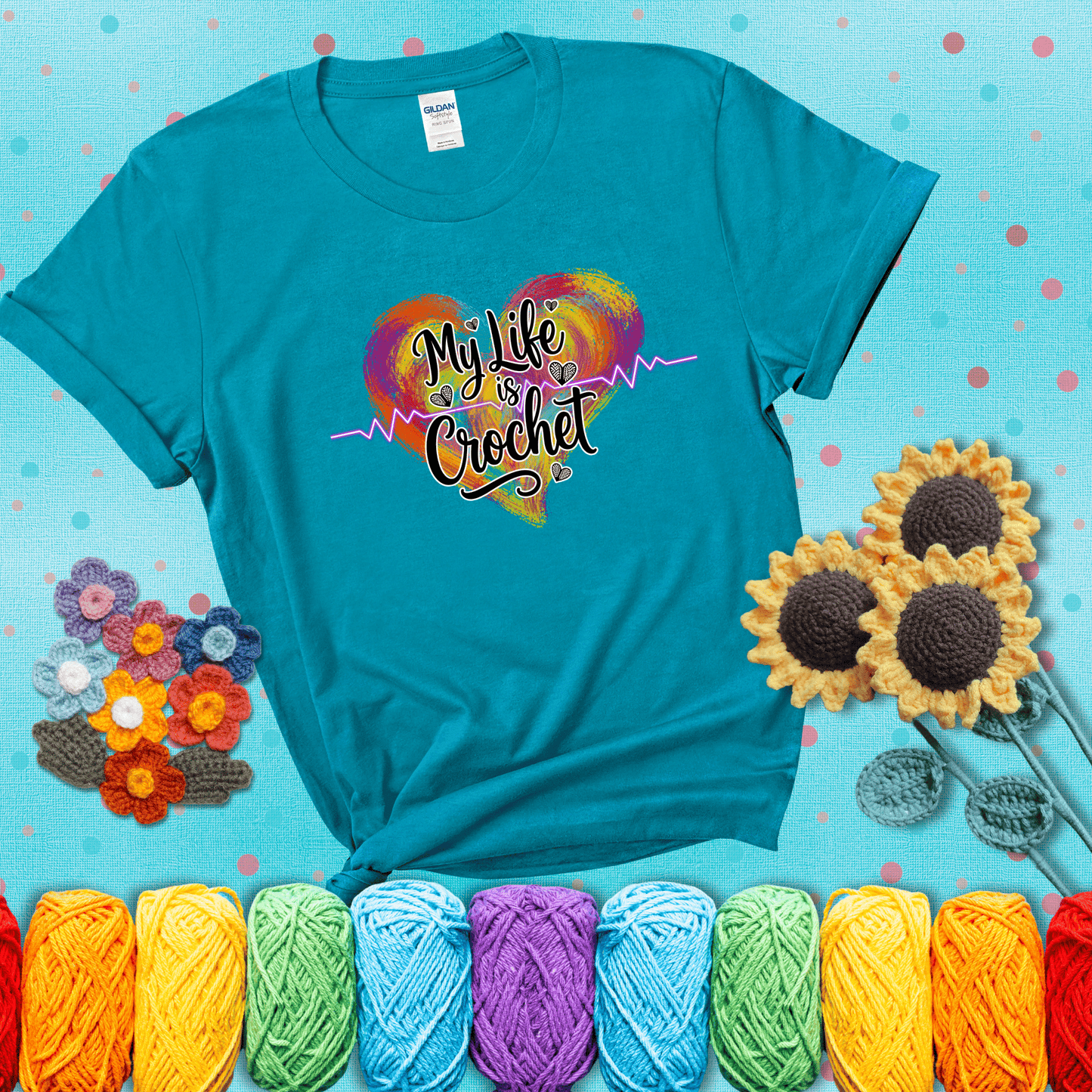 Colorful heart with an EKG line and text: “My Life is Crochet” in bold script showing a blue-green tee with a teal sunflower background