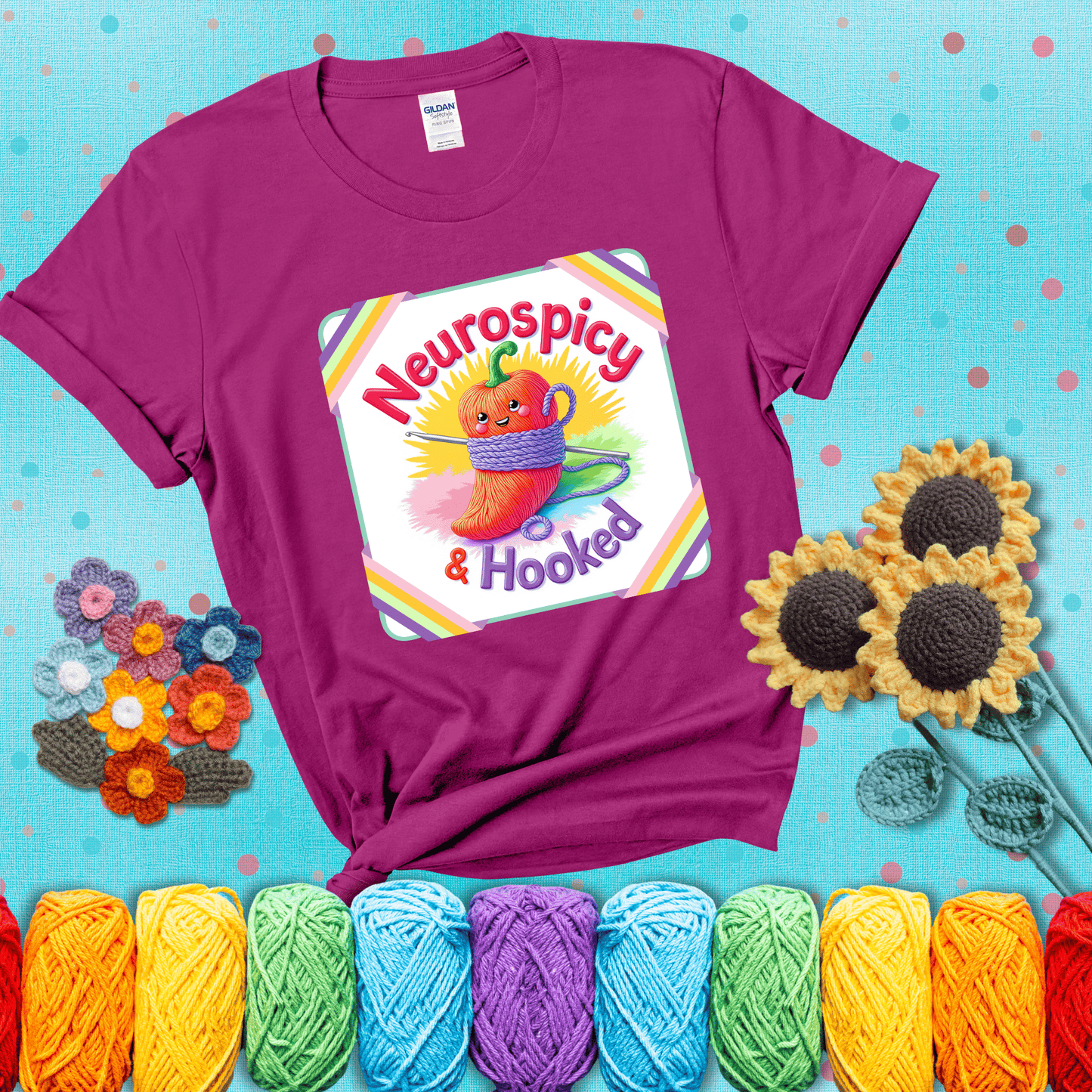 A cheerful red pepper wrapped in purple yarn with a crochet hook, framed by pastel rainbow corners and the words "Neurospicy & Hooked" showing a magenta tee with a teal sunflower background