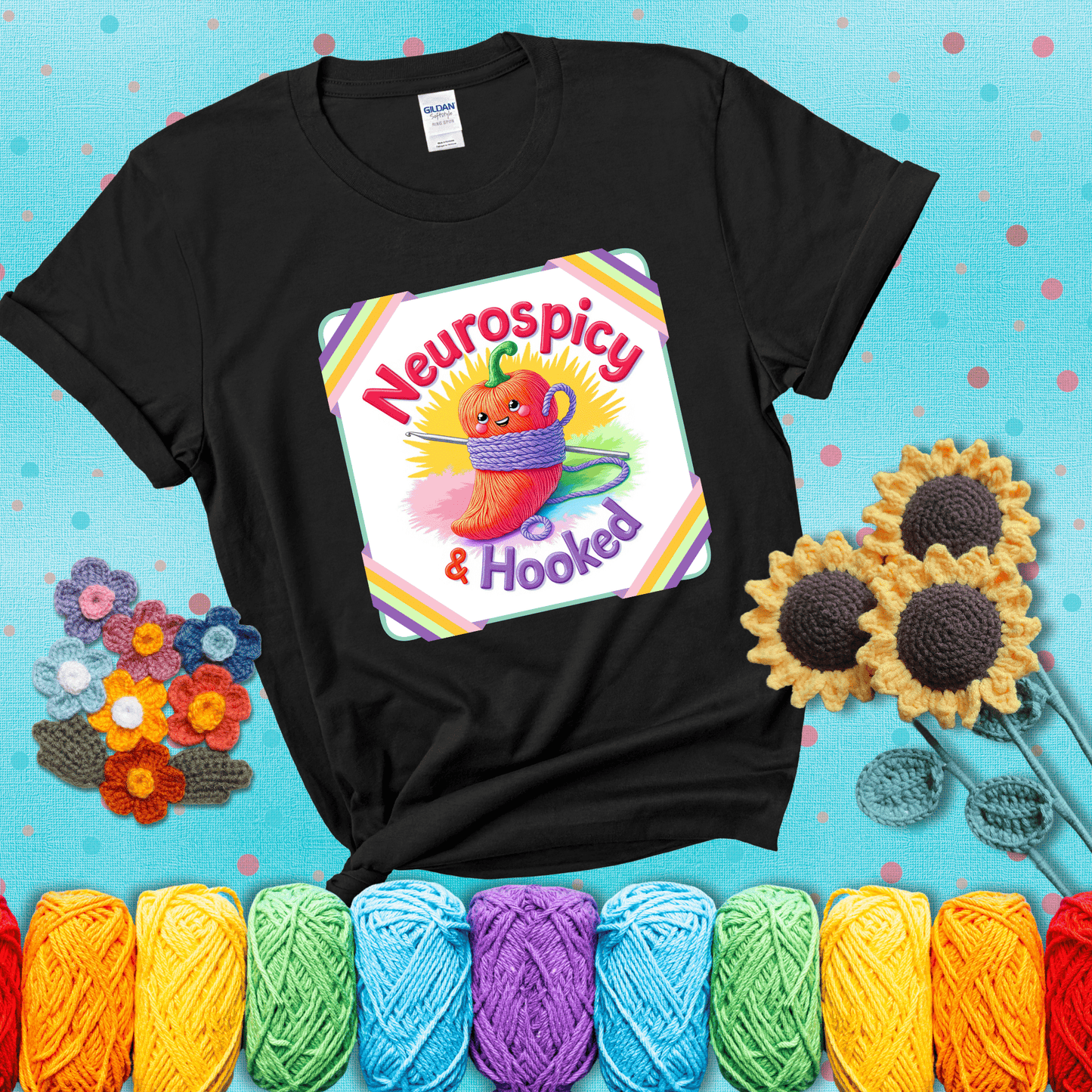 A cheerful red pepper wrapped in purple yarn with a crochet hook, framed by pastel rainbow corners and the words "Neurospicy & Hooked" showing a black tee with a teal sunflower background