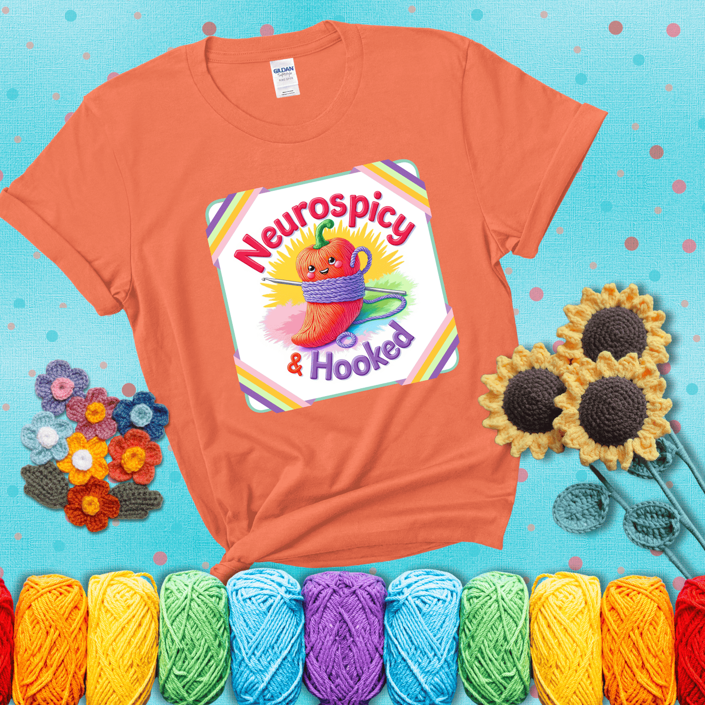 A cheerful red pepper wrapped in purple yarn with a crochet hook, framed by pastel rainbow corners and the words "Neurospicy & Hooked" showing a light orange tee with a teal sunflower background