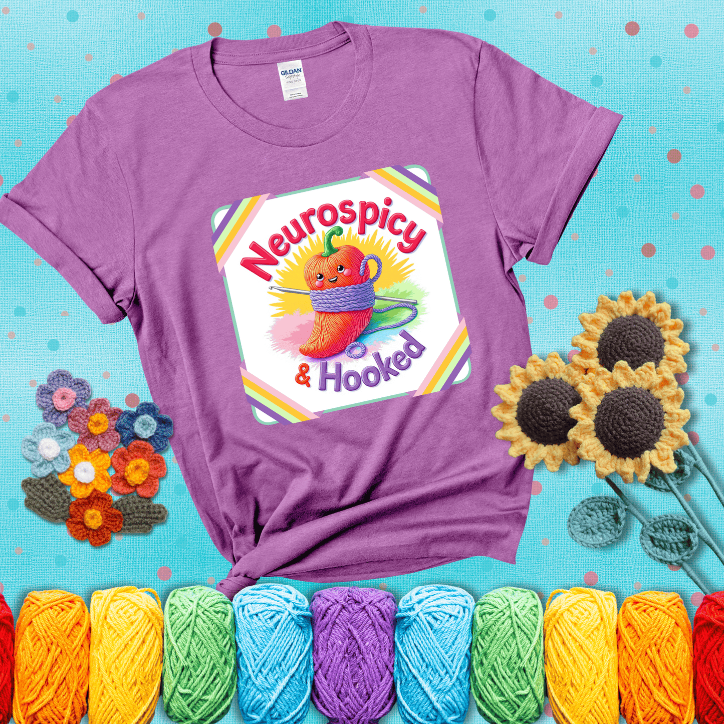 A cheerful red pepper wrapped in purple yarn with a crochet hook, framed by pastel rainbow corners and the words "Neurospicy & Hooked" showing a light purple tee with a teal sunflower background