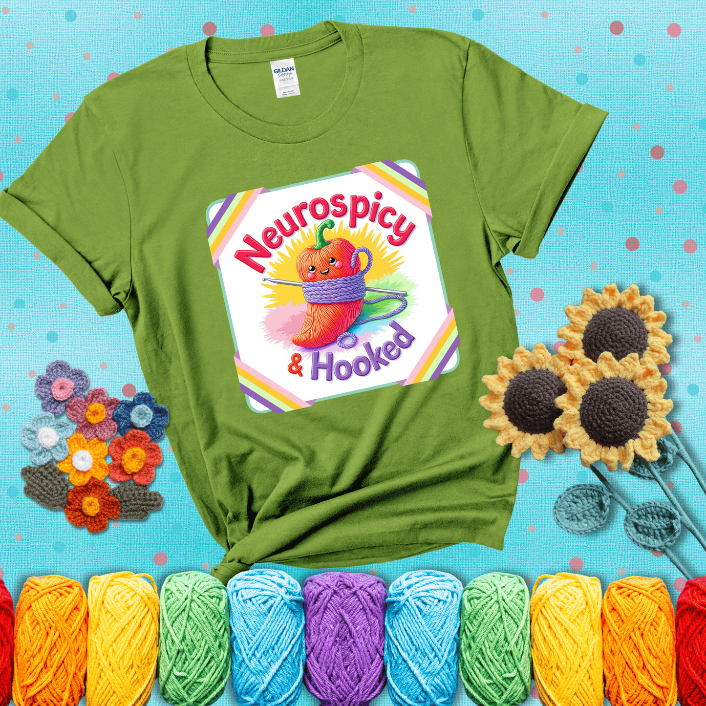 A cheerful red pepper wrapped in purple yarn with a crochet hook, framed by pastel rainbow corners and the words "Neurospicy & Hooked" showing a bright green tee with a teal sunflower background