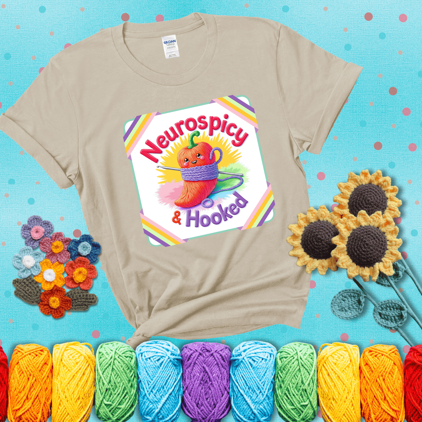 A cheerful red pepper wrapped in purple yarn with a crochet hook, framed by pastel rainbow corners and the words "Neurospicy & Hooked" showing a beige tee with a teal sunflower background