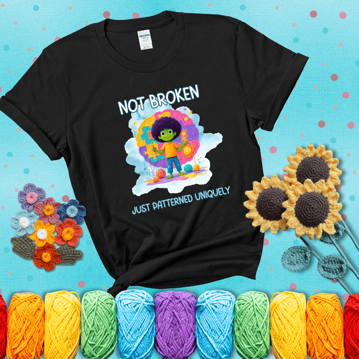 A smiling green character stands on a colorful crochet mat shaped like puzzle pieces, holding yarn and a hook, with the words “Not broken, just patterned uniquely” showing a black tee with a teal sunflower background