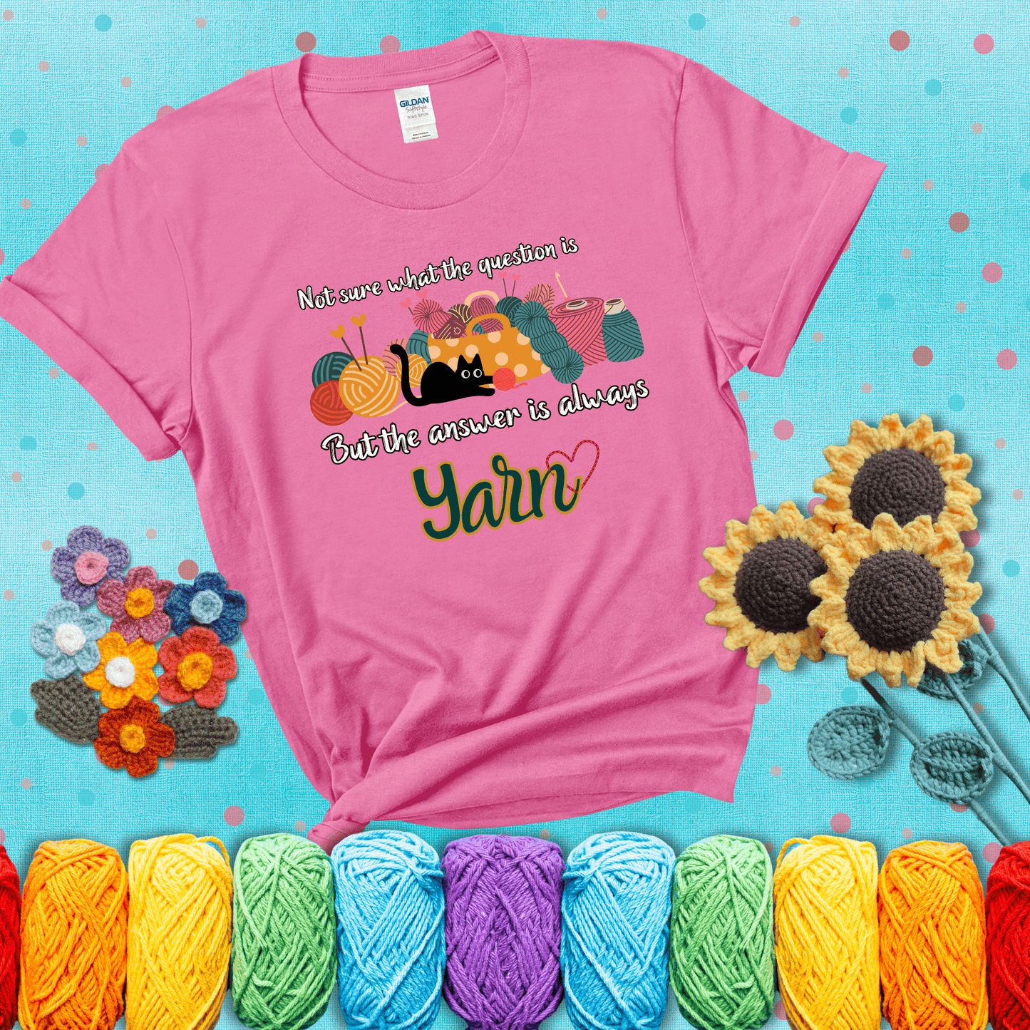 Illustration of a black cat playing with yarn next to a basket full of colorful skeins, with the phrase "Not sure what the question is, but the answer is always yarn" showing a pink tee with a teal sunflower background