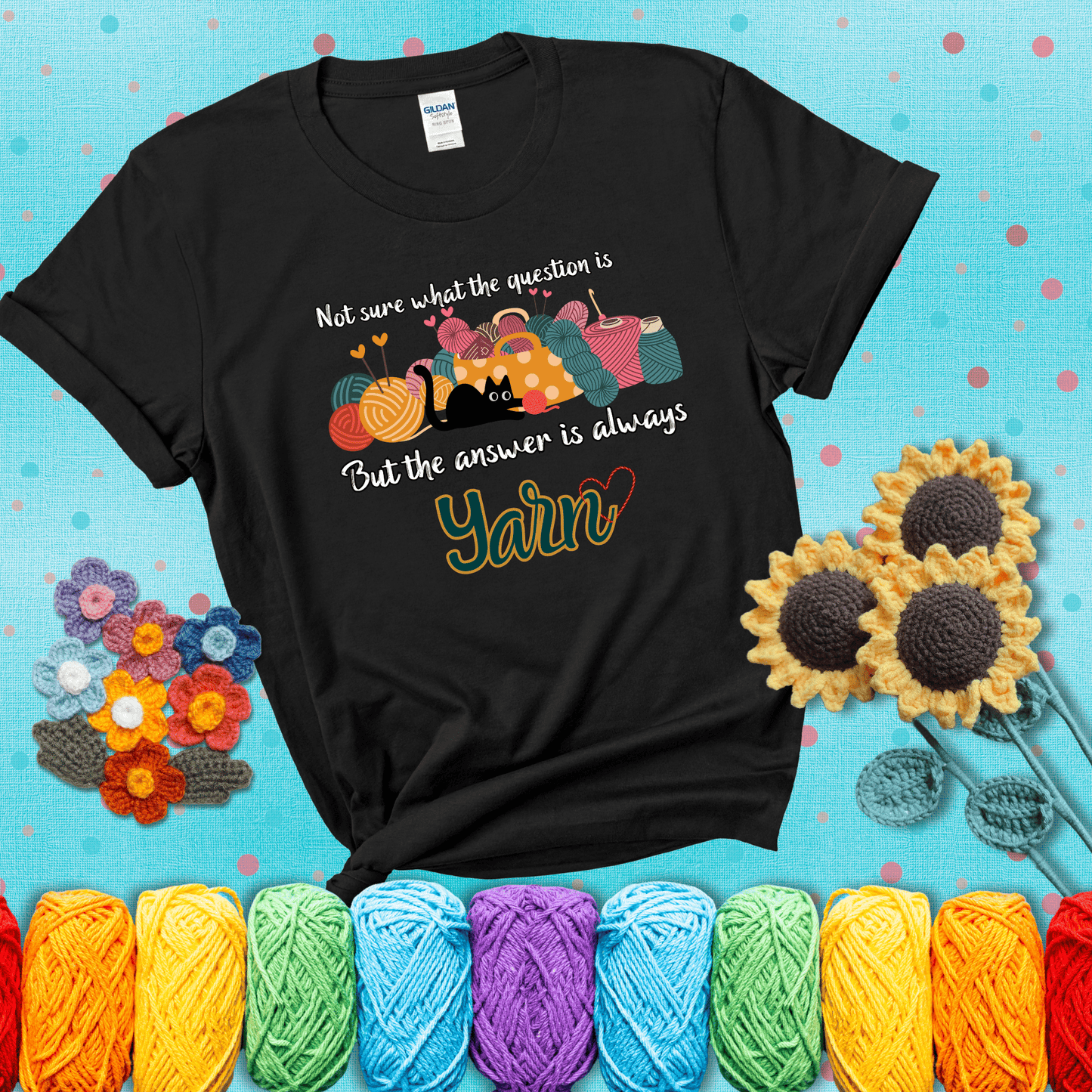 Illustration of a black cat playing with yarn next to a basket full of colorful skeins, with the phrase "Not sure what the question is, but the answer is always yarn" showing a black tee with a teal sunflower background