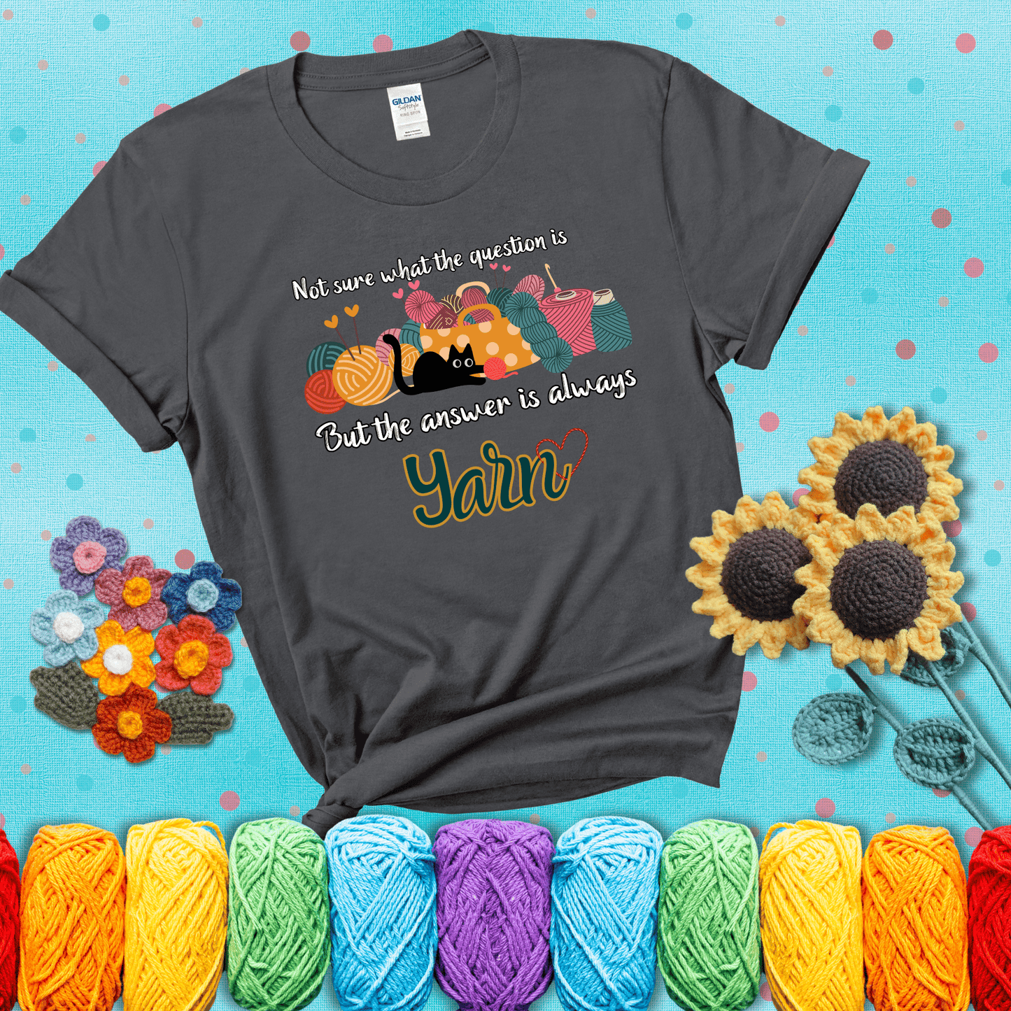 Illustration of a black cat playing with yarn next to a basket full of colorful skeins, with the phrase "Not sure what the question is, but the answer is always yarn" showing a dark grey tee with a teal sunflower background