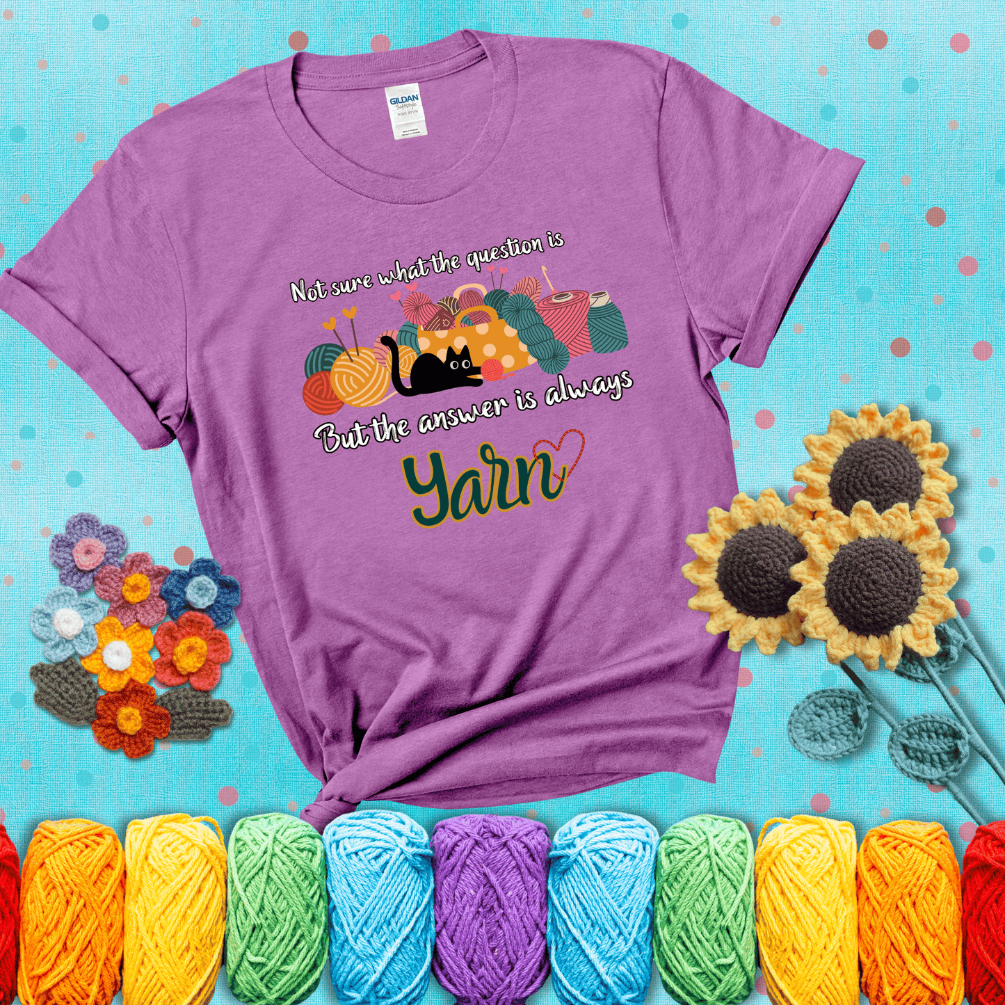 Illustration of a black cat playing with yarn next to a basket full of colorful skeins, with the phrase "Not sure what the question is, but the answer is always yarn" showing a light purple tee with a teal sunflower background