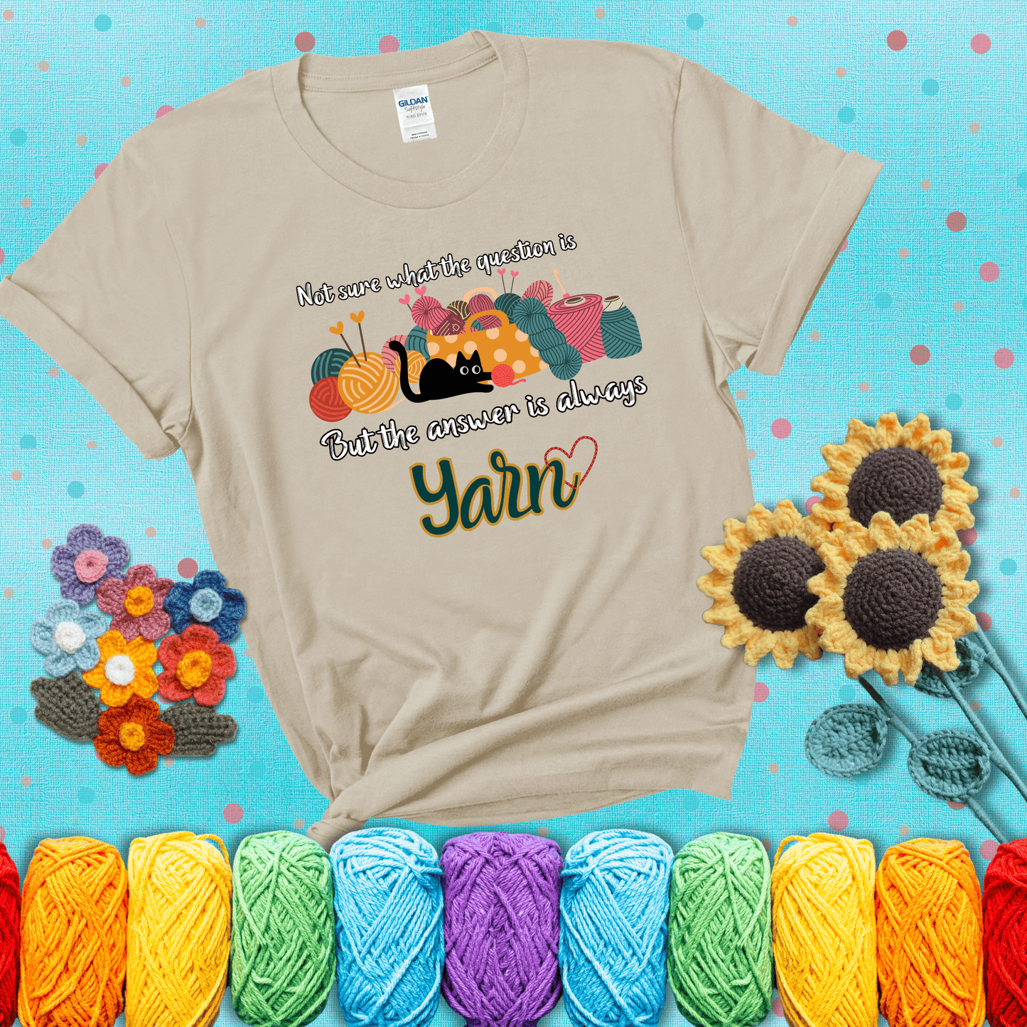 Illustration of a black cat playing with yarn next to a basket full of colorful skeins, with the phrase "Not sure what the question is, but the answer is always yarn" showing a beige tee with a teal sunflower background