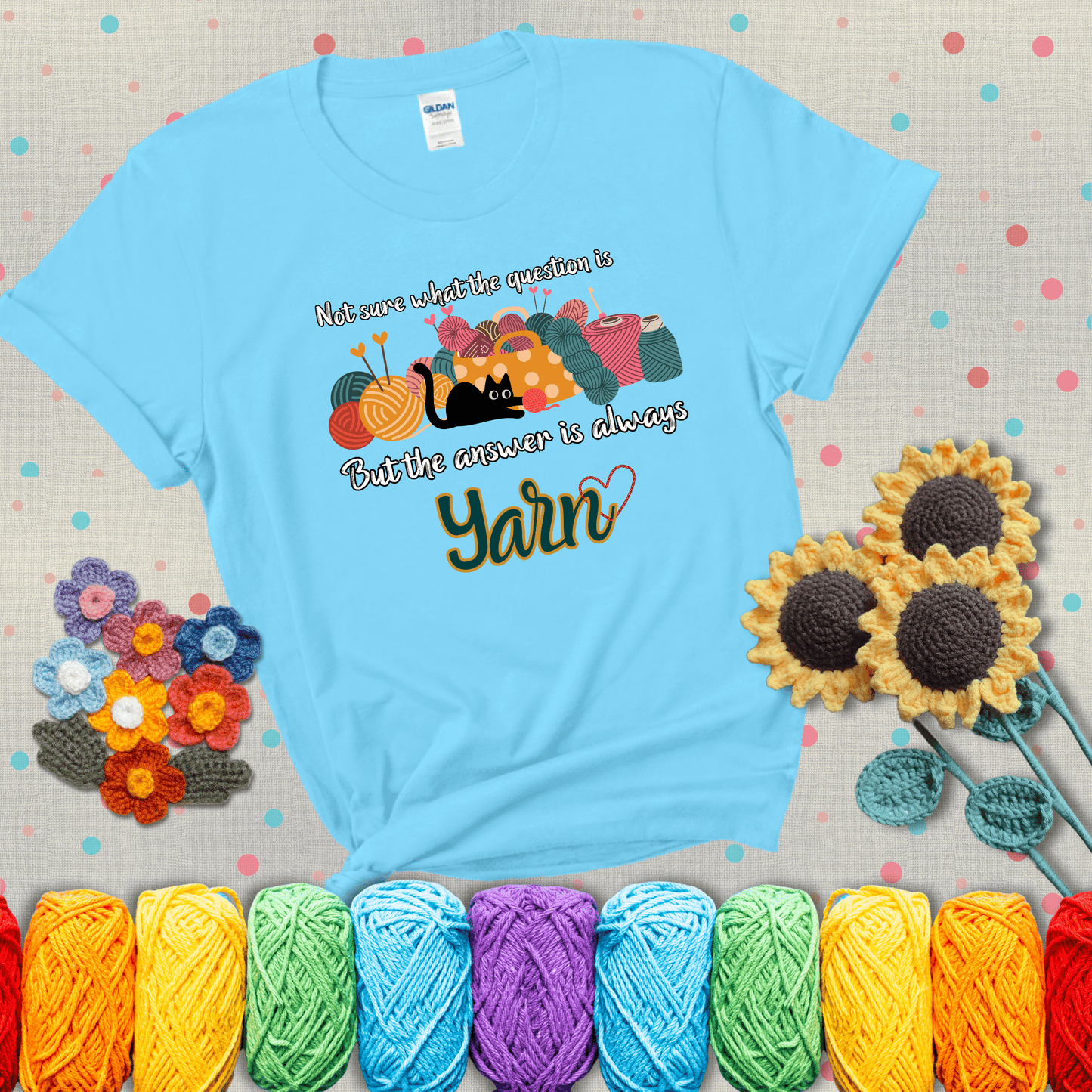 Illustration of a black cat playing with yarn next to a basket full of colorful skeins, with the phrase "Not sure what the question is, but the answer is always yarn" showing a blue-green tee with a teal sunflower background