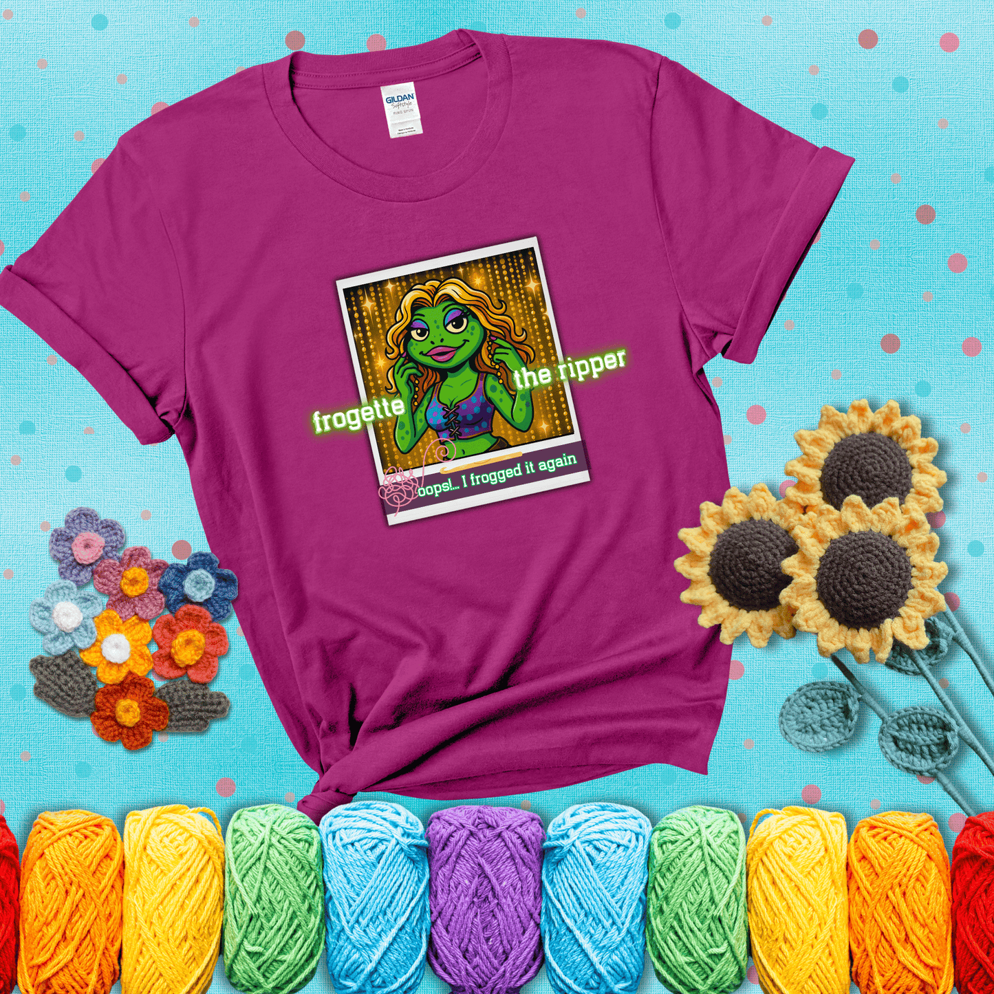 Retro-styled illustration of a glamorous green frog in a sparkly outfit, labeled "Frogette the Ripper" with the phrase “Oops! I frogged it again” below, referencing both crochet and pop culture showing a magenta tee with a teal sunflower background