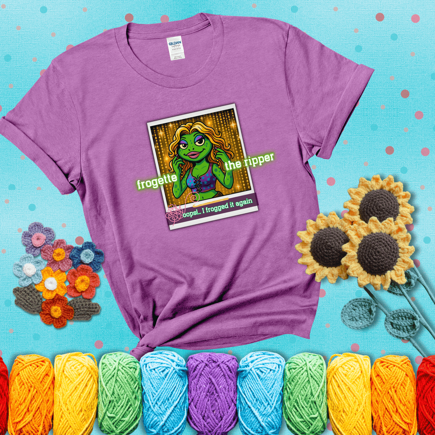 Retro-styled illustration of a glamorous green frog in a sparkly outfit, labeled "Frogette the Ripper" with the phrase “Oops! I frogged it again” below, referencing both crochet and pop culture showing a light purple tee with a teal sunflower background