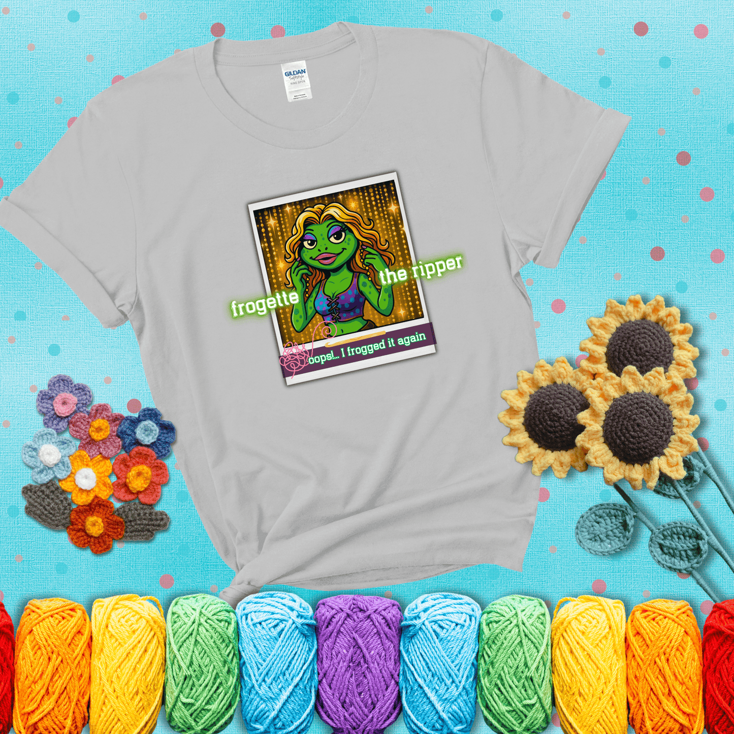 Retro-styled illustration of a glamorous green frog in a sparkly outfit, labeled "Frogette the Ripper" with the phrase “Oops! I frogged it again” below, referencing both crochet and pop culture showing a light grey tee with a teal sunflower background