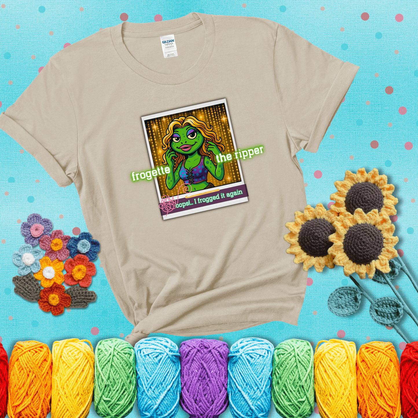 Retro-styled illustration of a glamorous green frog in a sparkly outfit, labeled "Frogette the Ripper" with the phrase “Oops! I frogged it again” below, referencing both crochet and pop culture showing a beige tee with a teal sunflower background