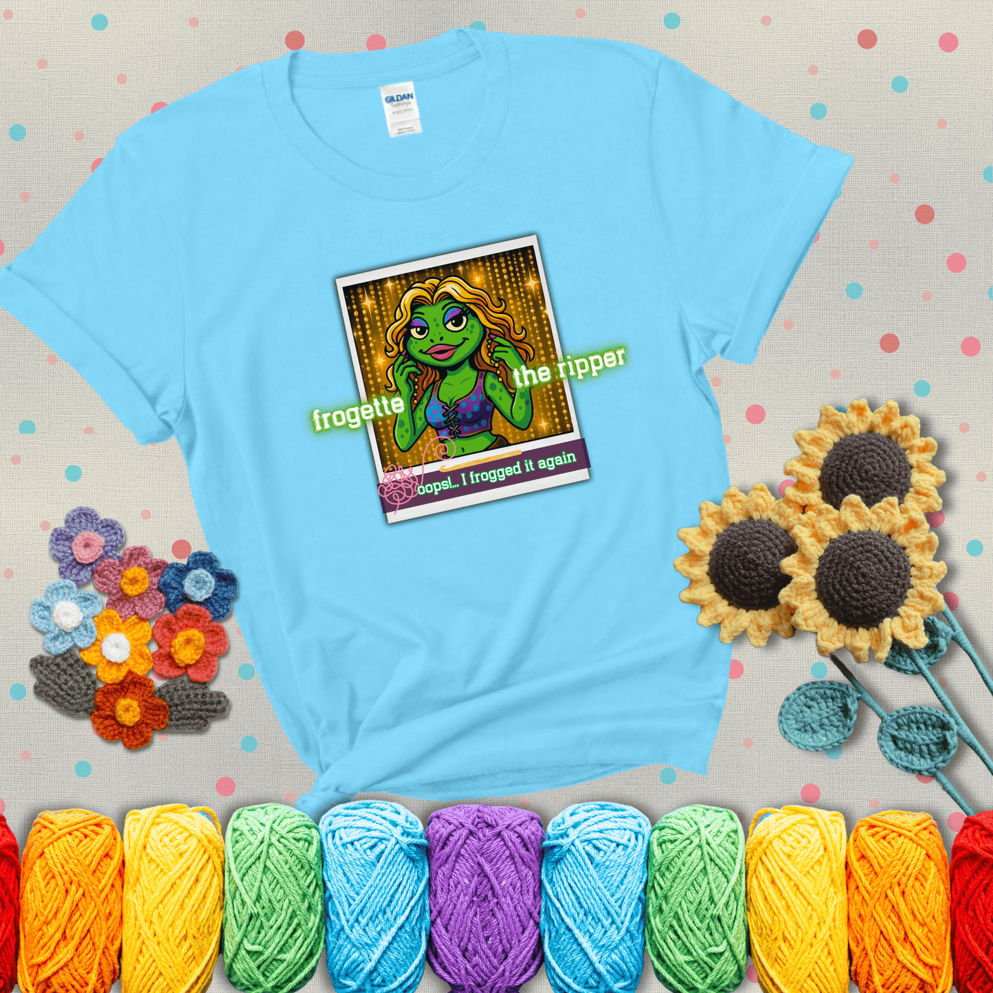 Retro-styled illustration of a glamorous green frog in a sparkly outfit, labeled "Frogette the Ripper" with the phrase “Oops! I frogged it again” below, referencing both crochet and pop culture showing a light blue tee with grey sunflower background