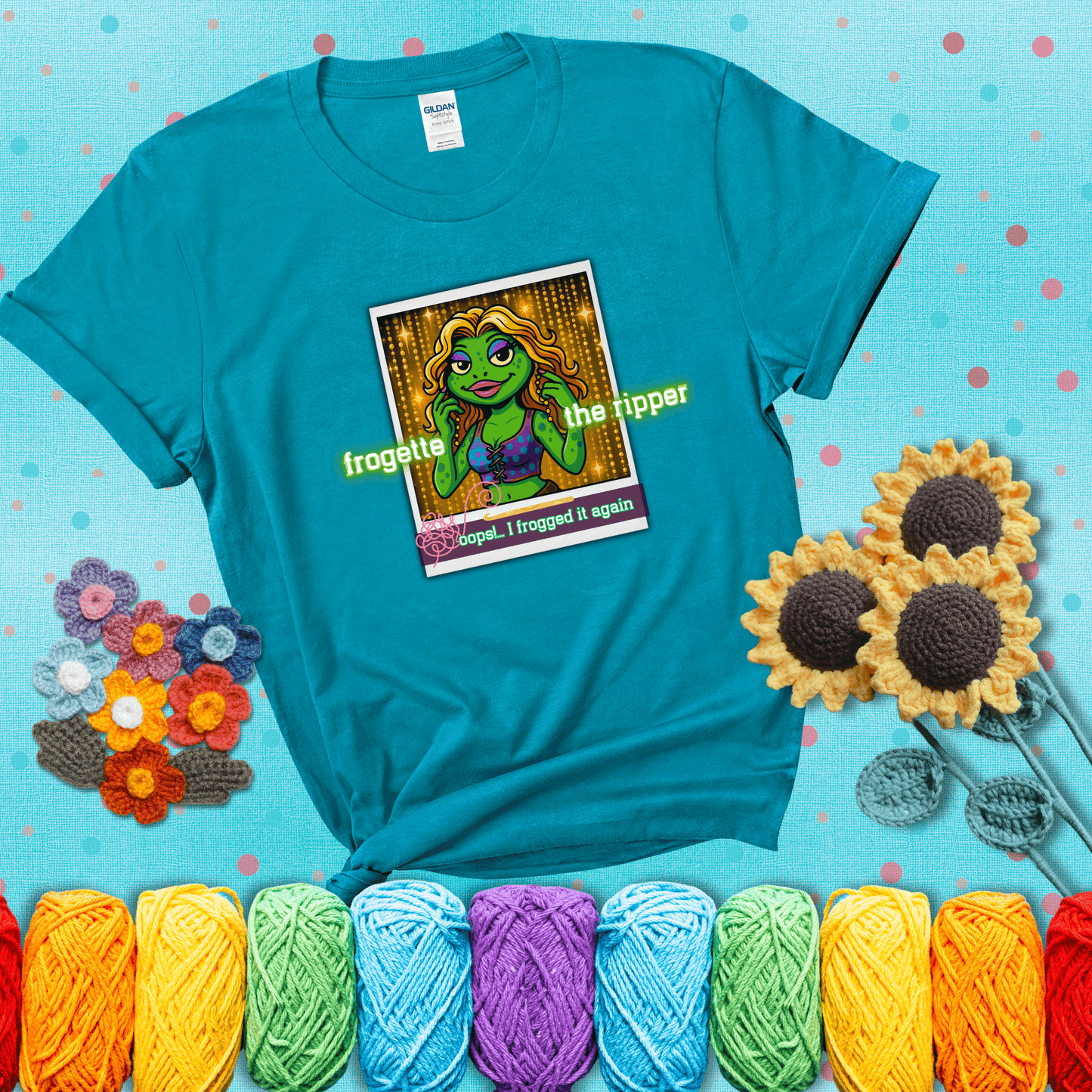 Retro-styled illustration of a glamorous green frog in a sparkly outfit, labeled "Frogette the Ripper" with the phrase “Oops! I frogged it again” below, referencing both crochet and pop culture showing a blue-green tee with a teal sunflower background