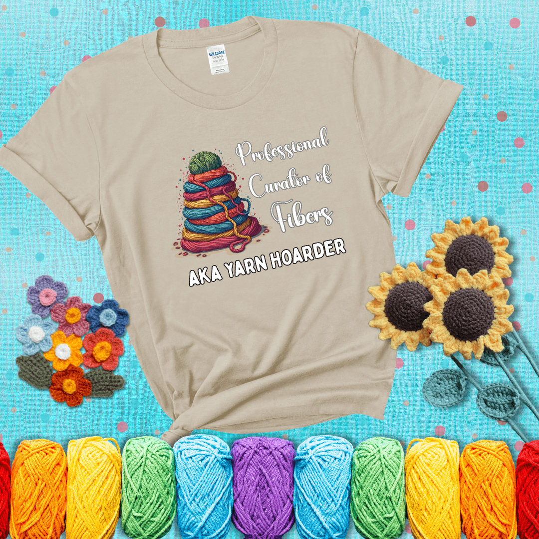 Pyramid of rainbow yarn topped with green ball; text reads “Professional Curator of Fibers AKA Yarn Hoarder,” a playful shirt for serious stashers showing a beige tee with a teal sunflower background