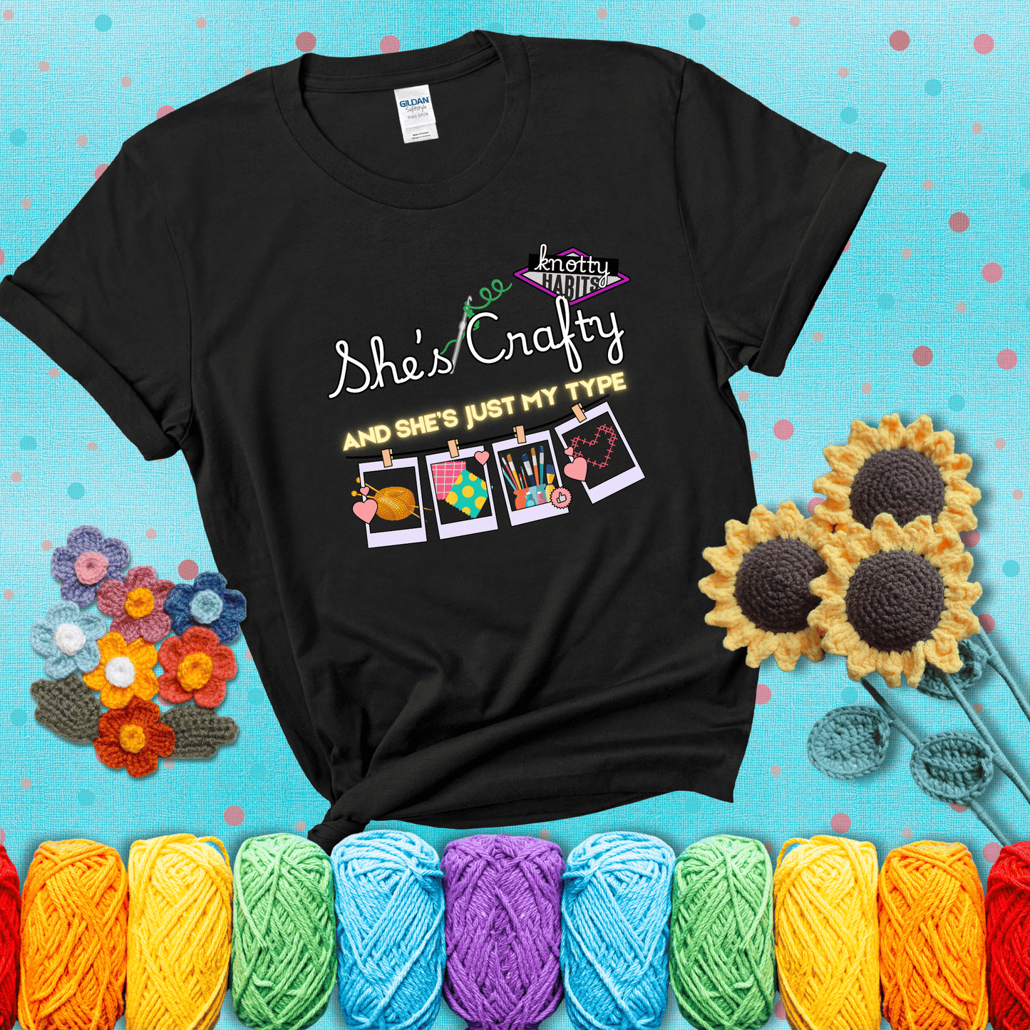 Text reads "She’s Crafty & She’s Just My Type" with yarn, fabric, painting, and cross-stitch icons hanging like Polaroids showing a black tee with a teal sunflower background