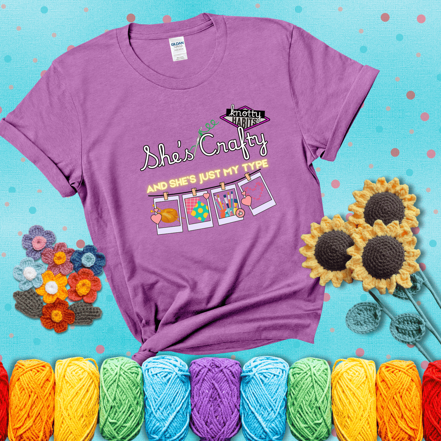 Text reads "She’s Crafty & She’s Just My Type" with yarn, fabric, painting, and cross-stitch icons hanging like Polaroids showing a light purple tee with a teal sunflower background