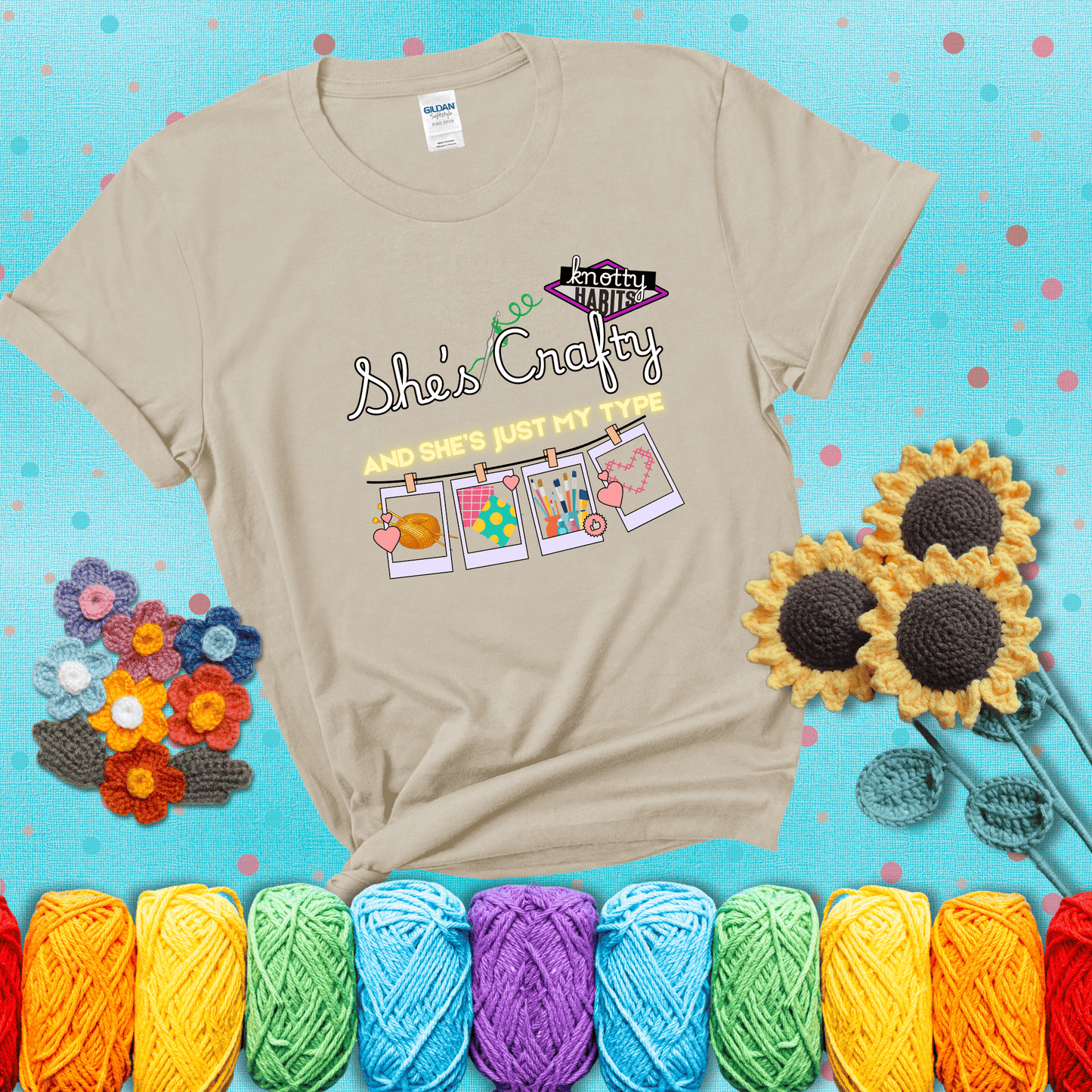 Text reads "She’s Crafty & She’s Just My Type" with yarn, fabric, painting, and cross-stitch icons hanging like Polaroids showing a beige tee with a teal sunflower background