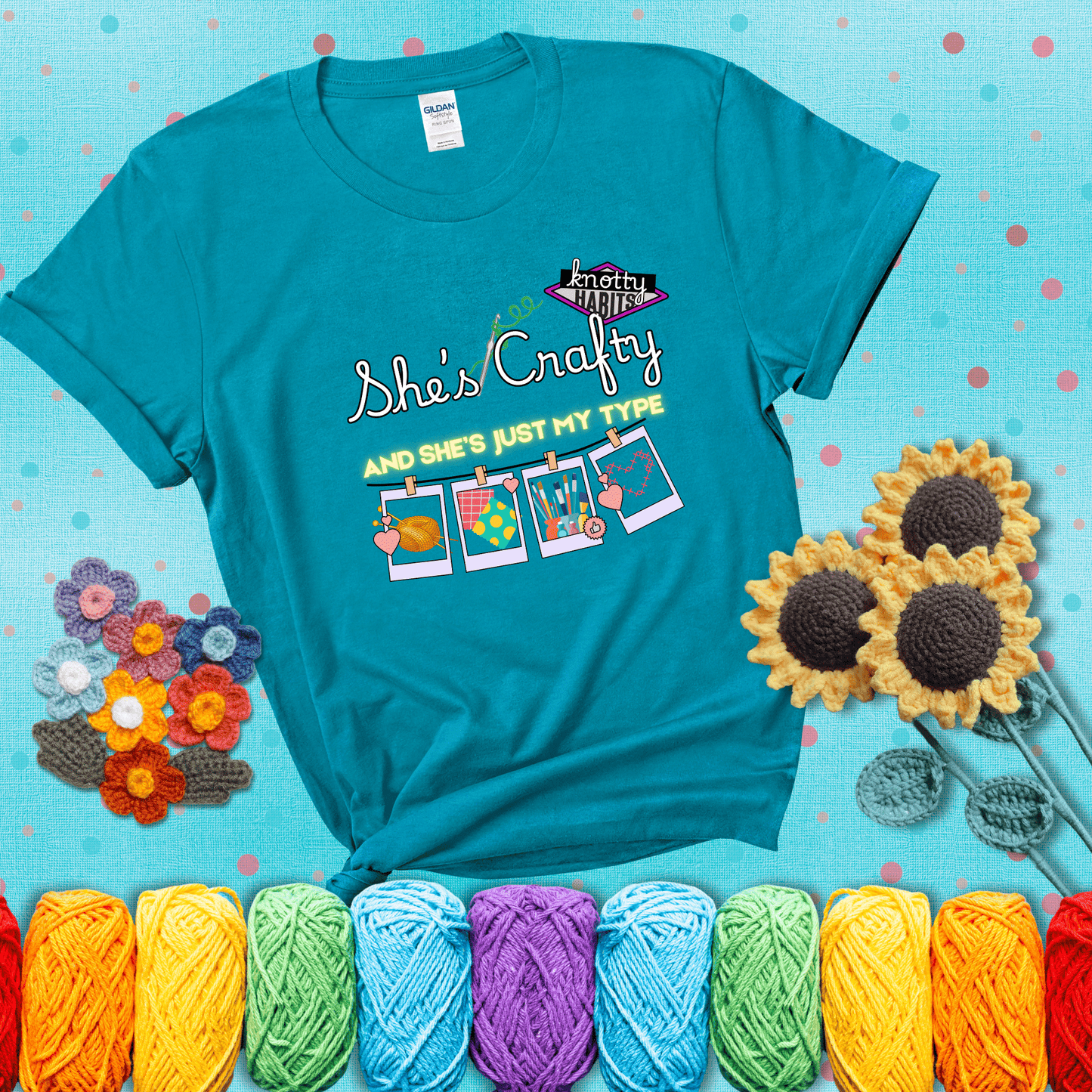 Text reads "She’s Crafty & She’s Just My Type" with yarn, fabric, painting, and cross-stitch icons hanging like Polaroids showing a blue-green tee with a teal sunflower background