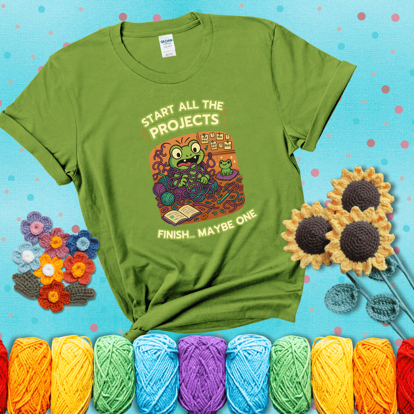 A wide-eyed crochet frog sits tangled in yarn with dozens of projects around, surrounded by chaos and “new project” notes. Caption reads “Start all the projects, finish... maybe one” showing a bright green tee with a teal sunflower background