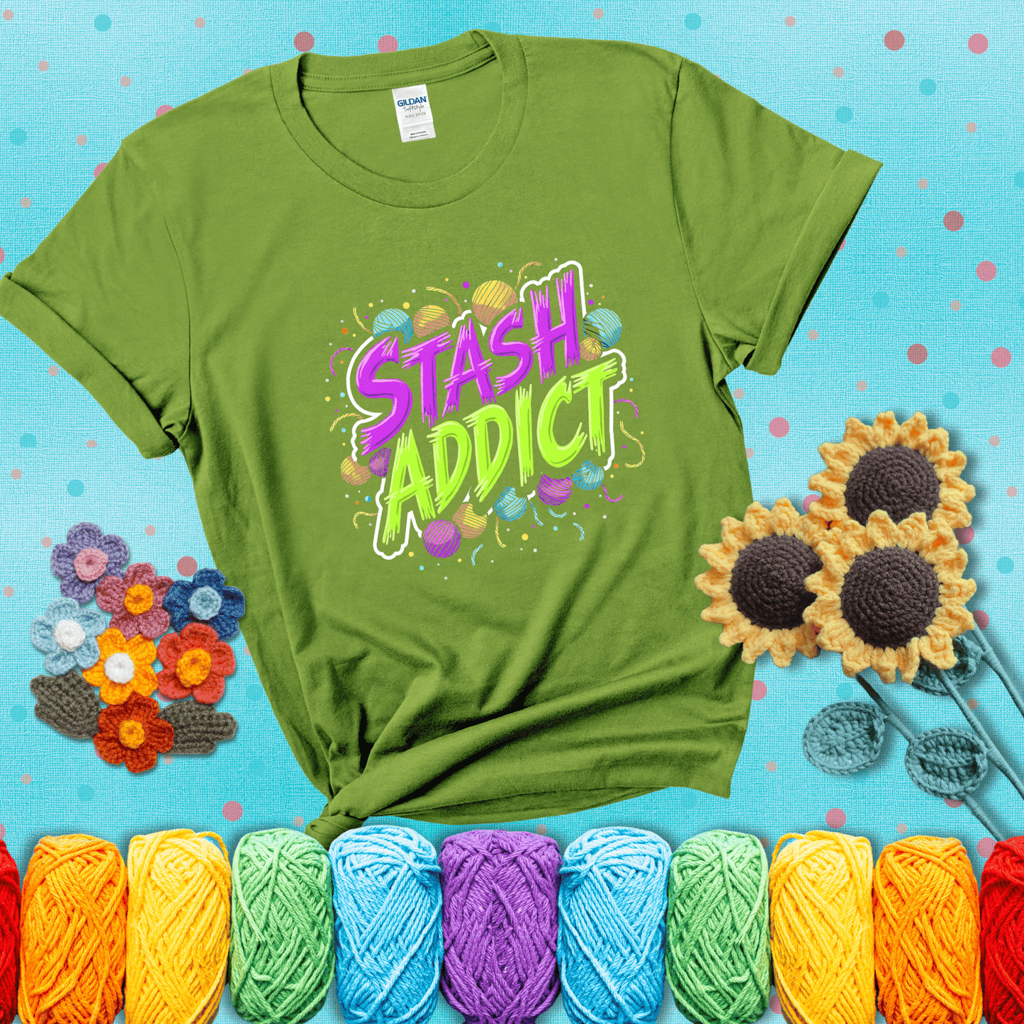 Bold neon text reading "Stash Addict" surrounded by colorful yarn balls and festive confetti on a neutral background showing a bright green tee with a teal sunflower background