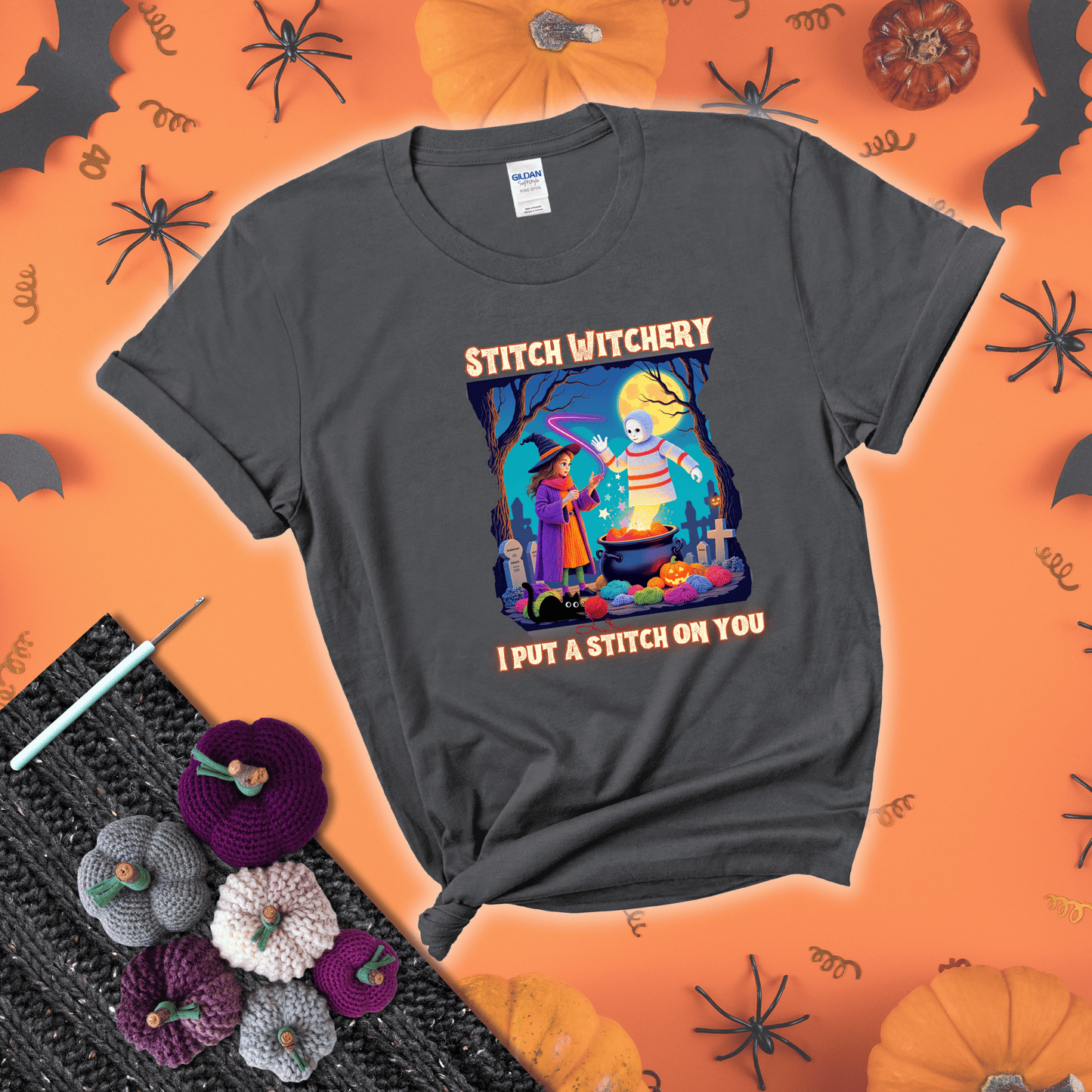 A Halloween scene with a young witch casting a yarn spell from a cauldron onto a floating crochet-ghost figure, under the phrase “I Put a Stitch on You” showing a dark grey tee with a festive Halloween background