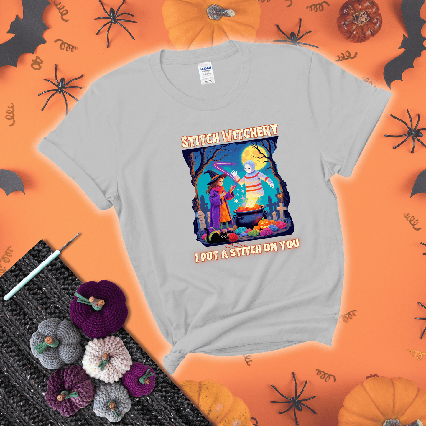 A Halloween scene with a young witch casting a yarn spell from a cauldron onto a floating crochet-ghost figure, under the phrase “I Put a Stitch on You” showing a light grey tee with a festive Halloween background