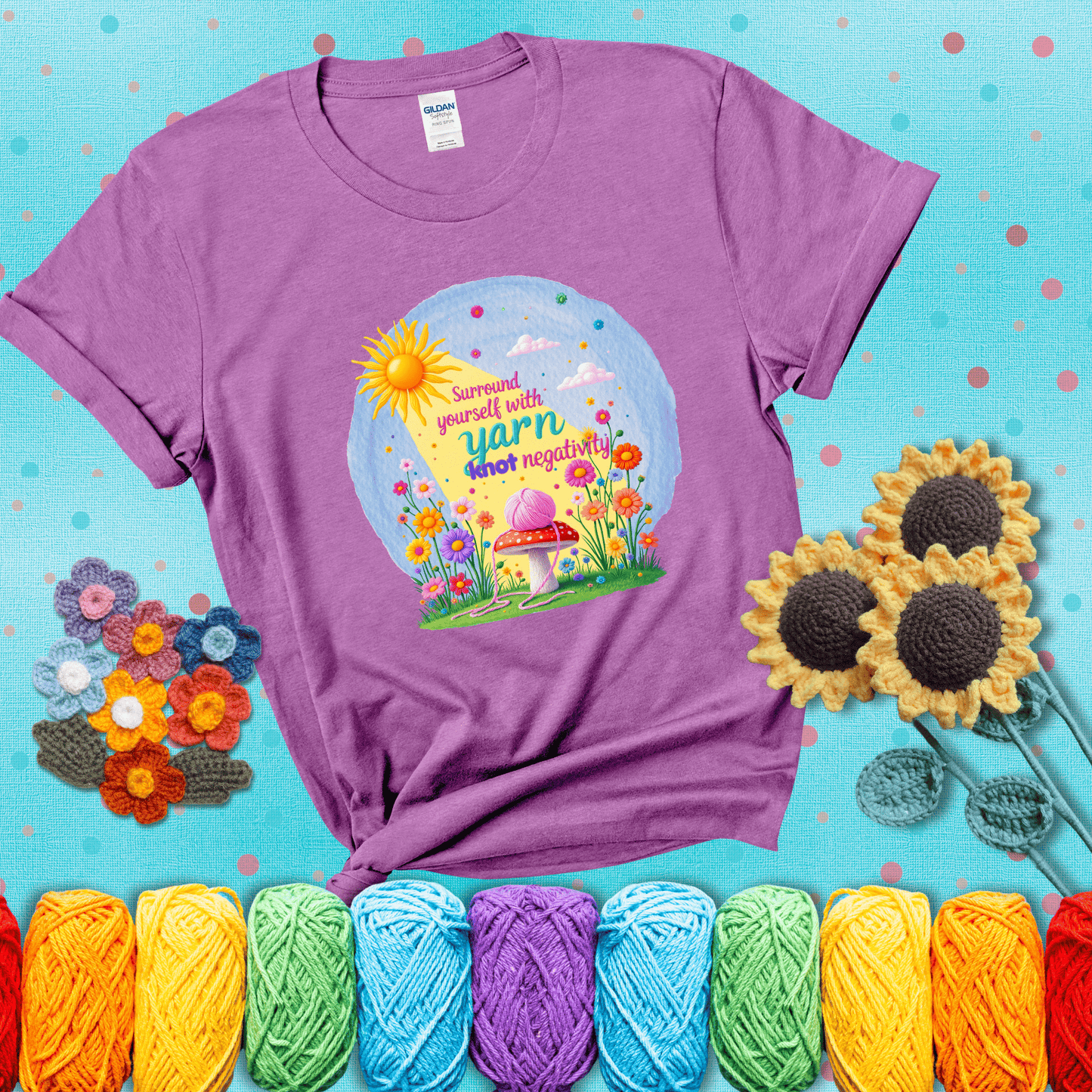 A happy spring garden scene with a sunbeam, flowers, and a pink yarn ball on a mushroom, with the quote "Surround yourself with yarn, knot negativity," showing a light purple tee with a teal sunflower background