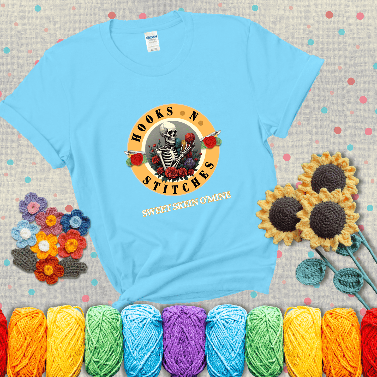 A skeleton holding colorful yarn, surrounded by roses, framed in a circular logo-style design that says “Hooks 'N Stitches” and “Sweet Skein O’Mine,” with crochet hooks piercing through showing a light blue tee with grey sunflower background