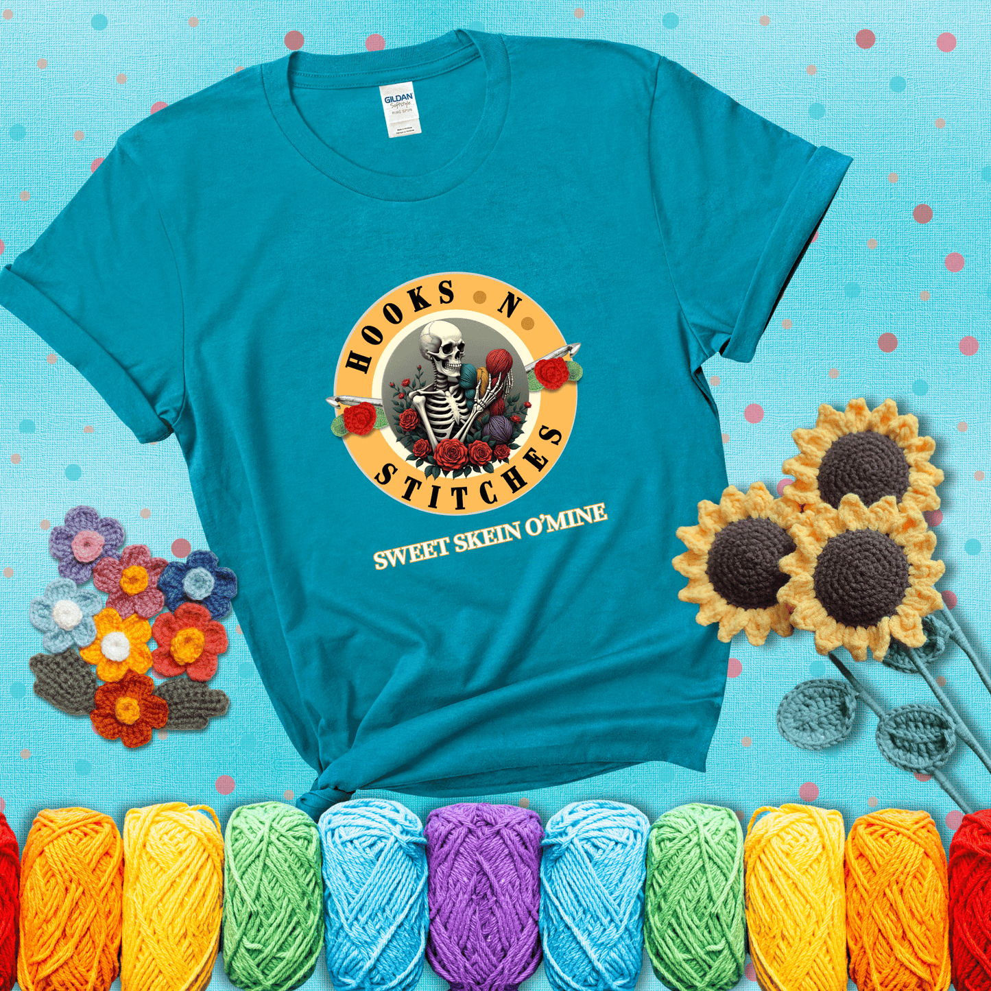 A skeleton holding colorful yarn, surrounded by roses, framed in a circular logo-style design that says “Hooks 'N Stitches” and “Sweet Skein O’Mine,” with crochet hooks piercing through showing a blue-green tee with a teal sunflower background