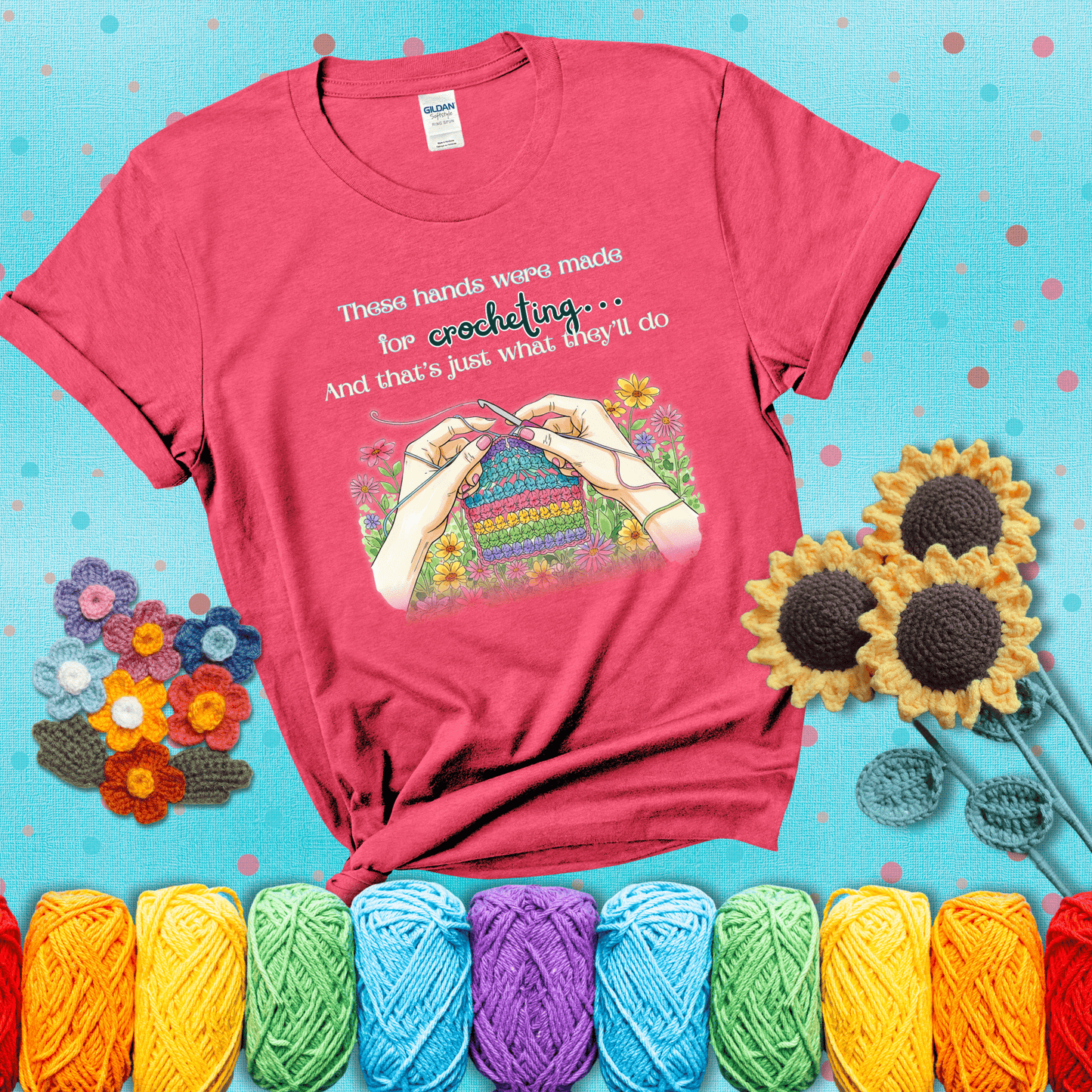 Illustration of two hands crocheting a rainbow swatch, surrounded by vibrant flowers with the phrase “These hands were made for crocheting… and that’s just what they’ll do,” showing a light red tee with a teal sunflower background