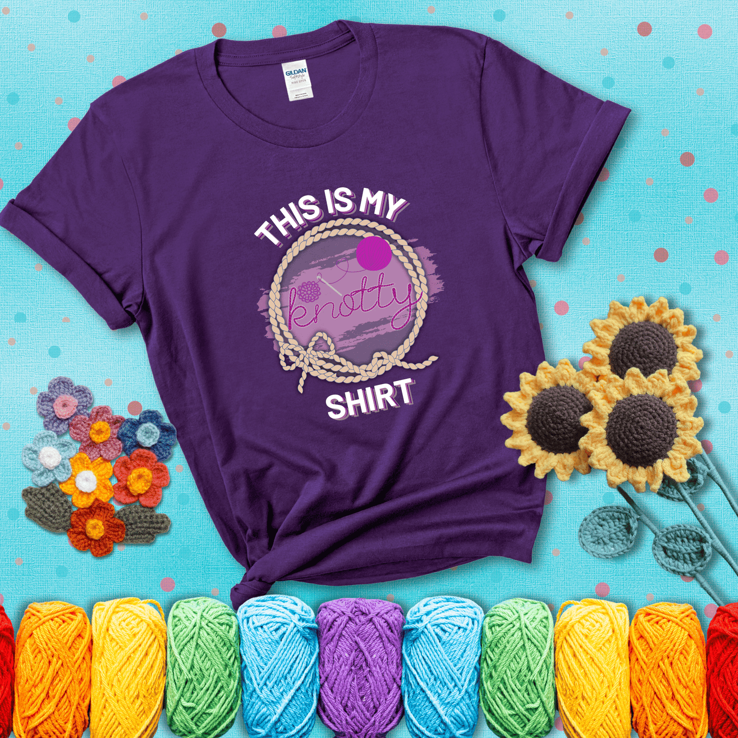 A playful design with the phrase "This is my knotty shirt" inside a rope circle, featuring a yarn ball and a crochet hook forming the word "knotty" showing a purple tee with a teal sunflower background